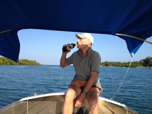 A man sitting at the bow of a boat with a canopy and drinking a beer.