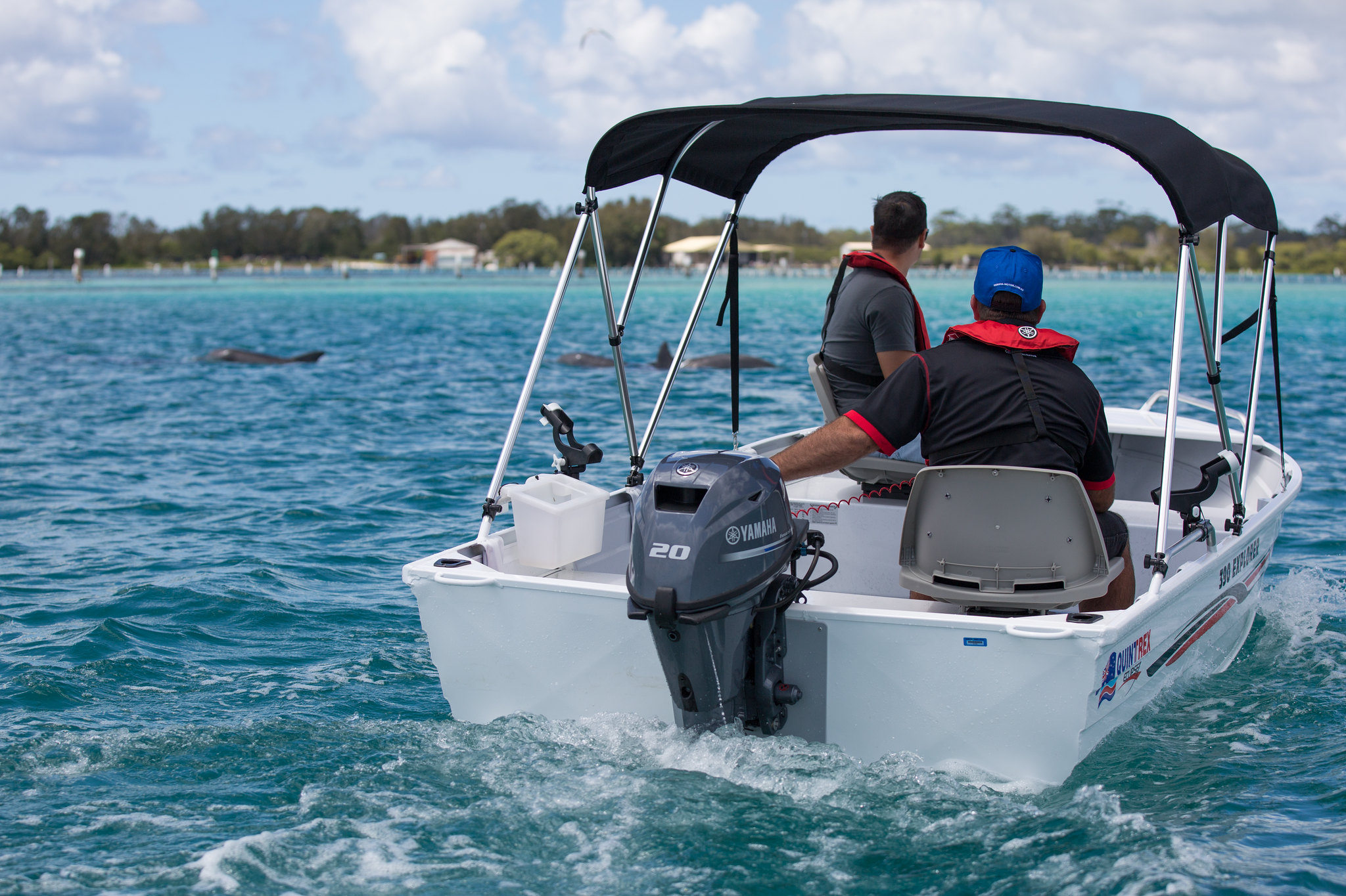 Two men aboard a small white boat with an outboard engine and a Bimini top attached.