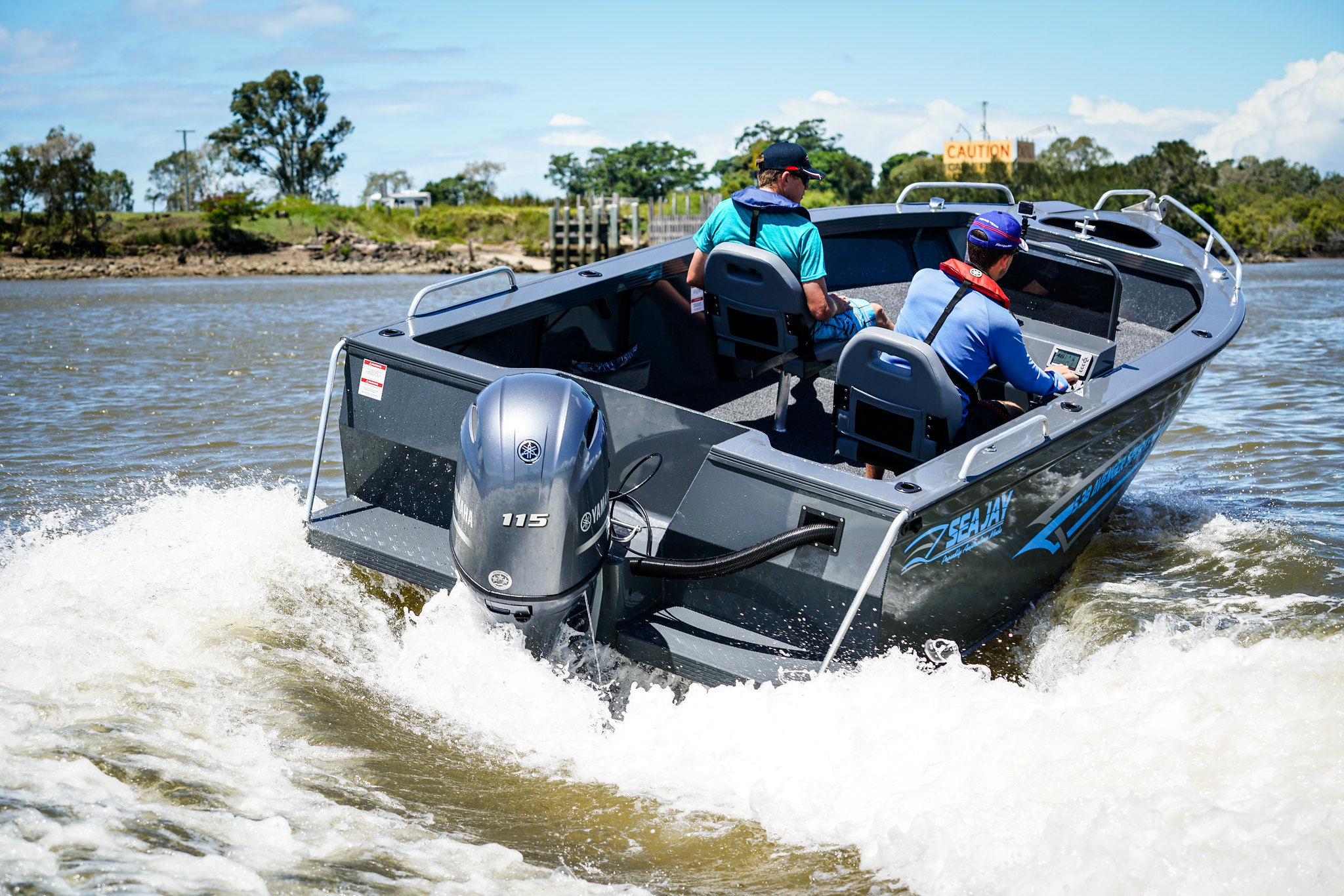 Two men operating a black open boat with an outboard motor at a lake.