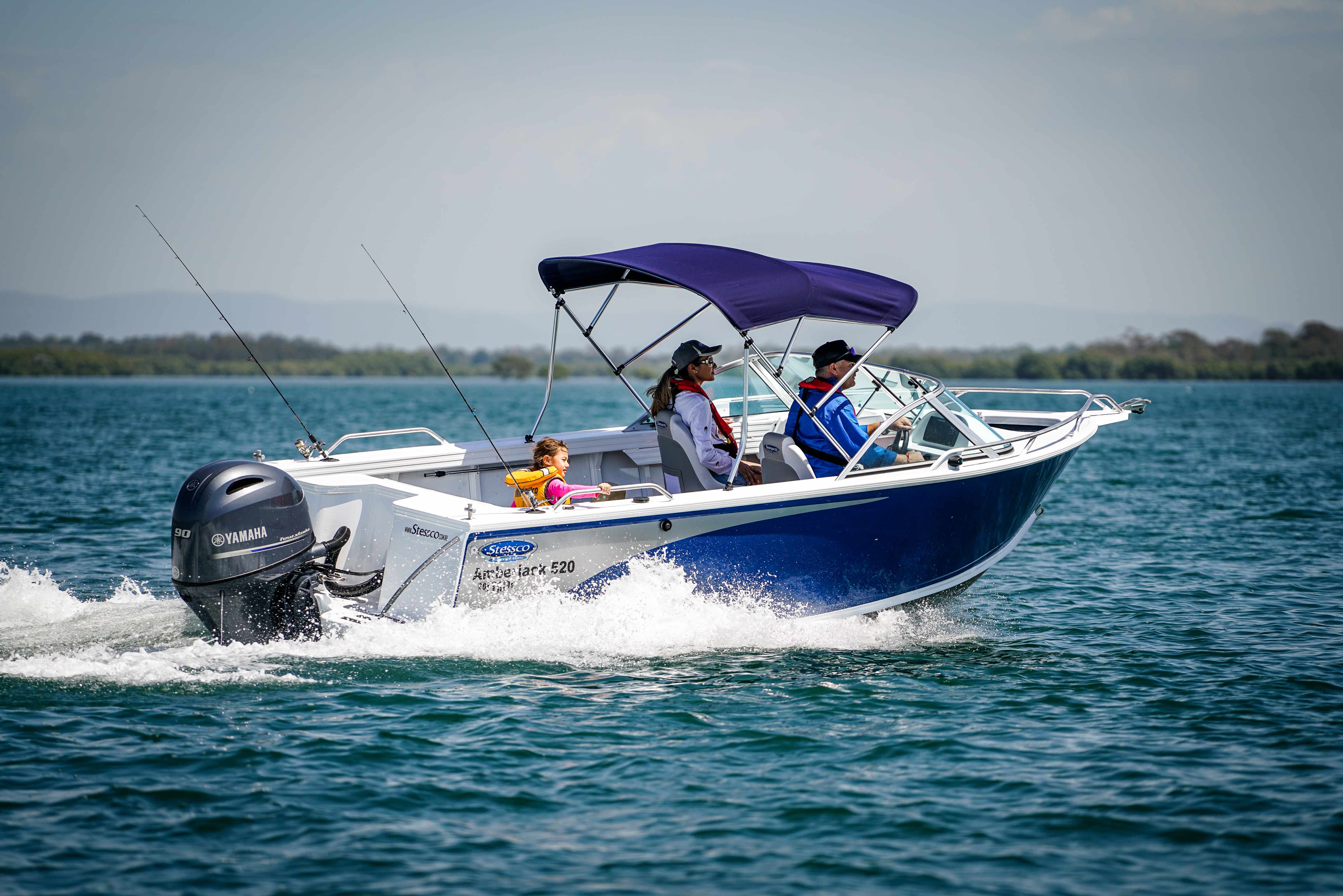 A family of three riding a blue moving boat with a blue Bimini top.