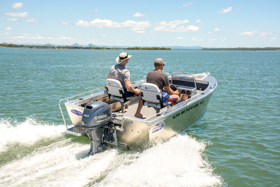 Two men sitting on individual boat chairs while operating the tinny boat as it's running on water.