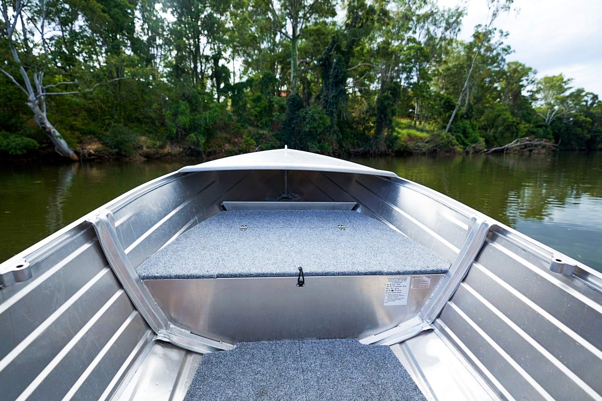 A small aluminium boat with grey marine carpet cruising along a lake.