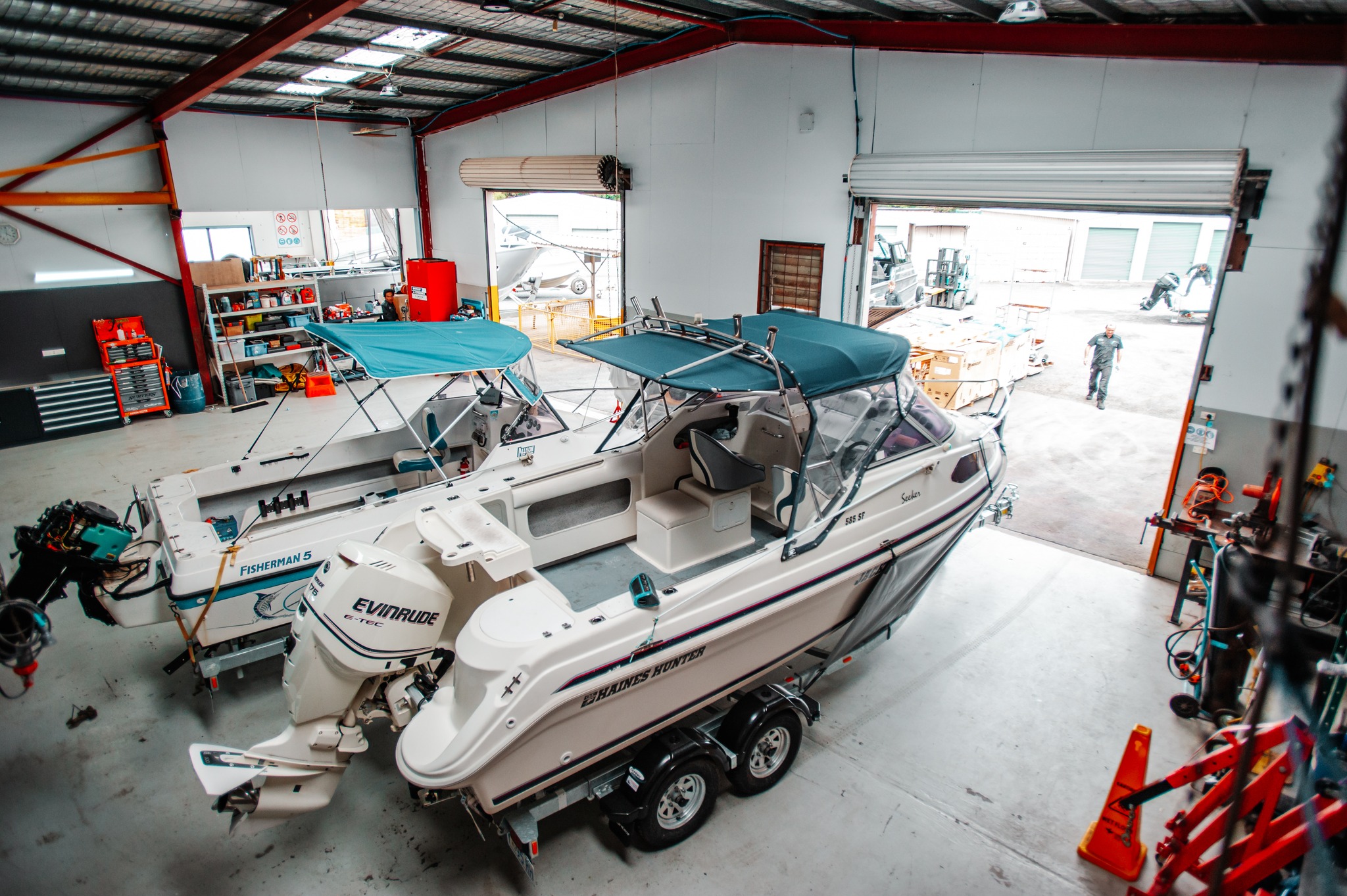 Two white boats with an outboard at the rear is stored inside a service shop.