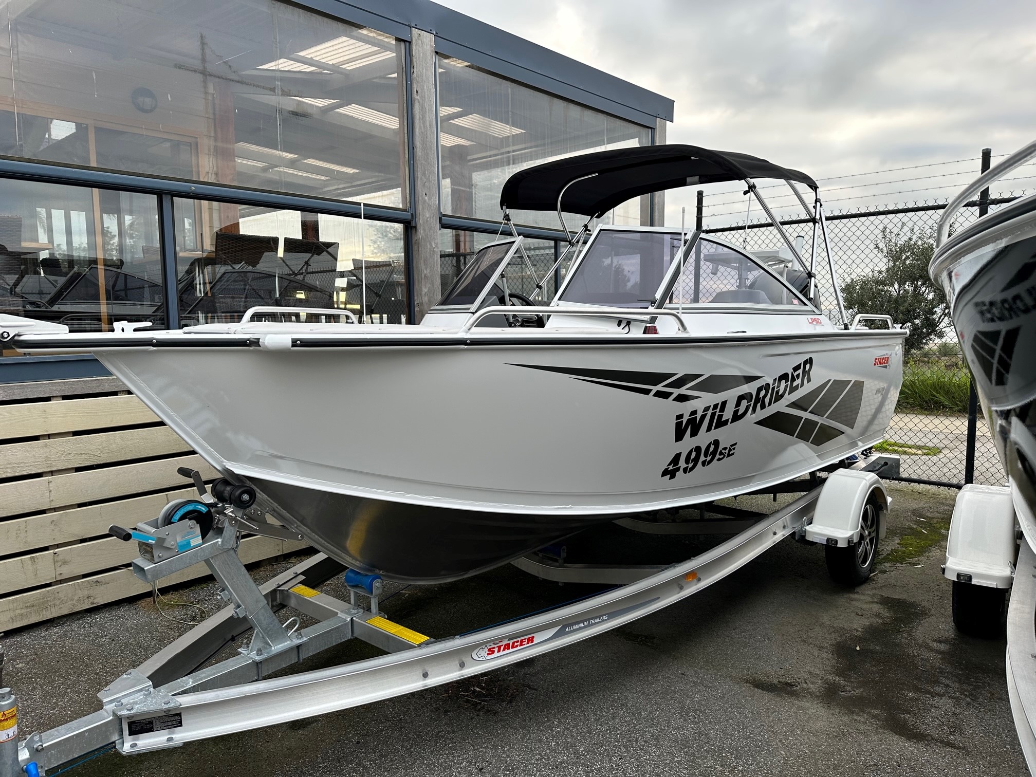 A Stacer Wildrider on a boat trailer is displayed in a dealership's parking area.