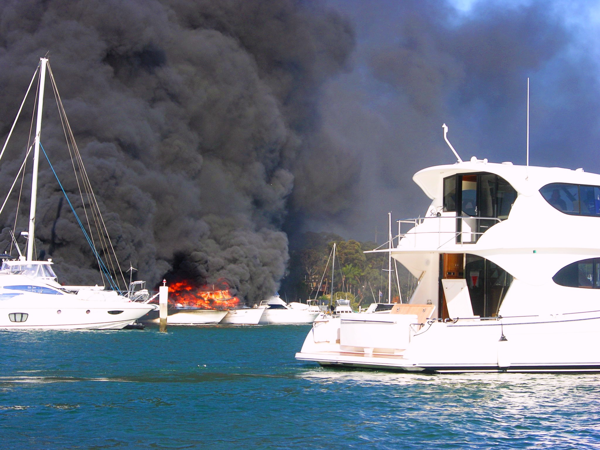 A wide angle shot of boats moored in a marina clouded with smoke and fire.