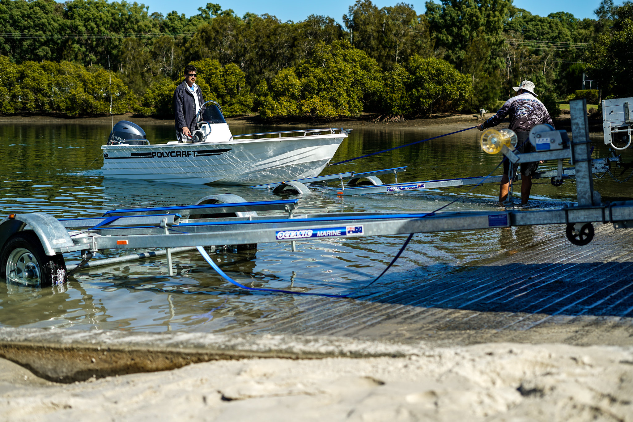 A man launching a boat using a trailer and a rope into the water.