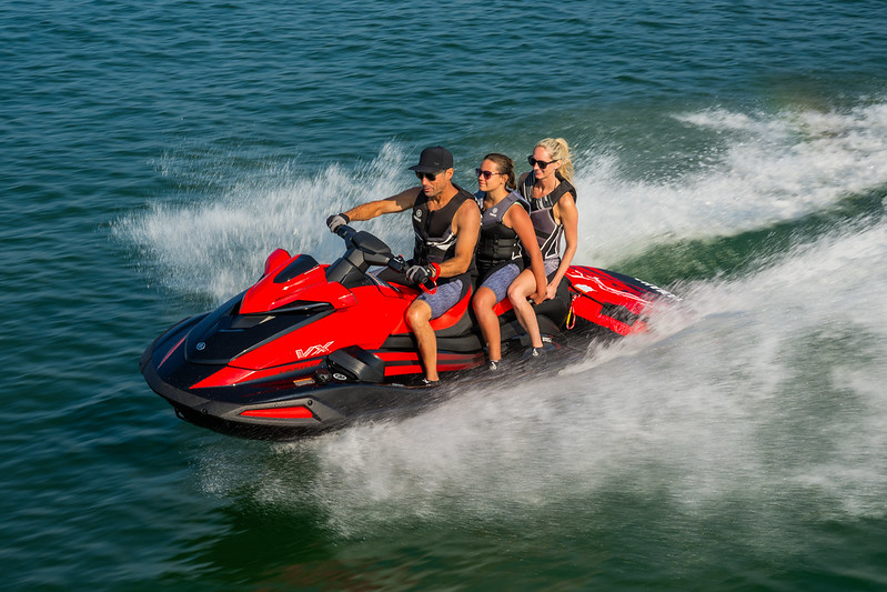 Three people riding a red jet ski.