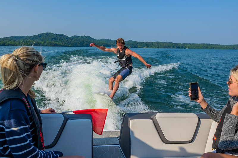 People onboard the boat observing and recording a man wakeboarding behind their boat.