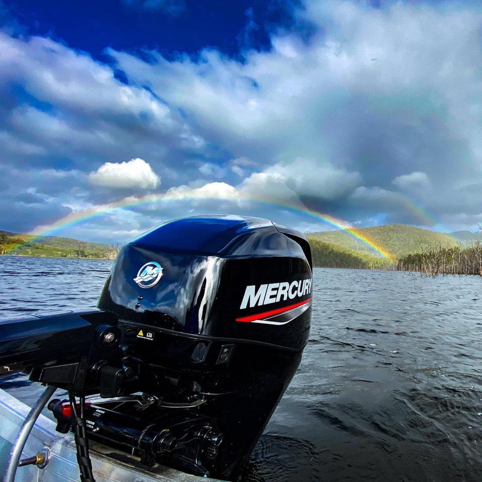 A close up shot of a Mercury outboard engine with a rainbow in the background.