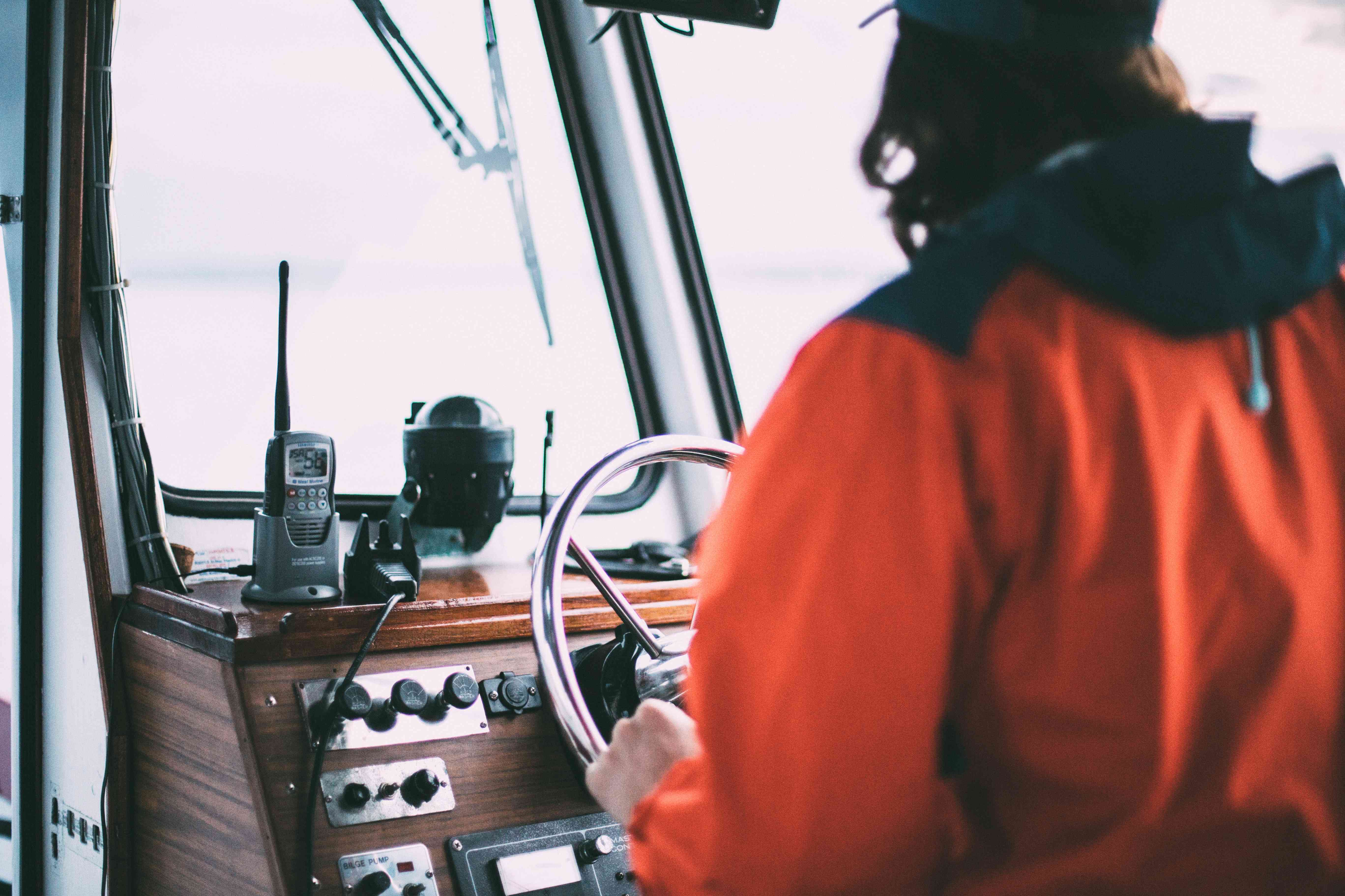 A marine radio placed on top of a console. A man is steering the boat's wheel.