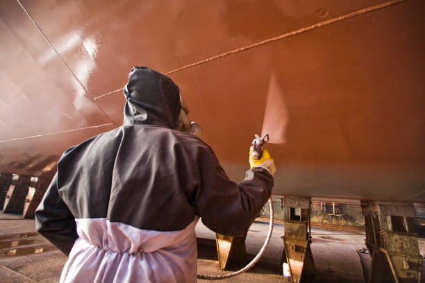 A man spraying antifouling red marine paint on a boat's bottom hull.