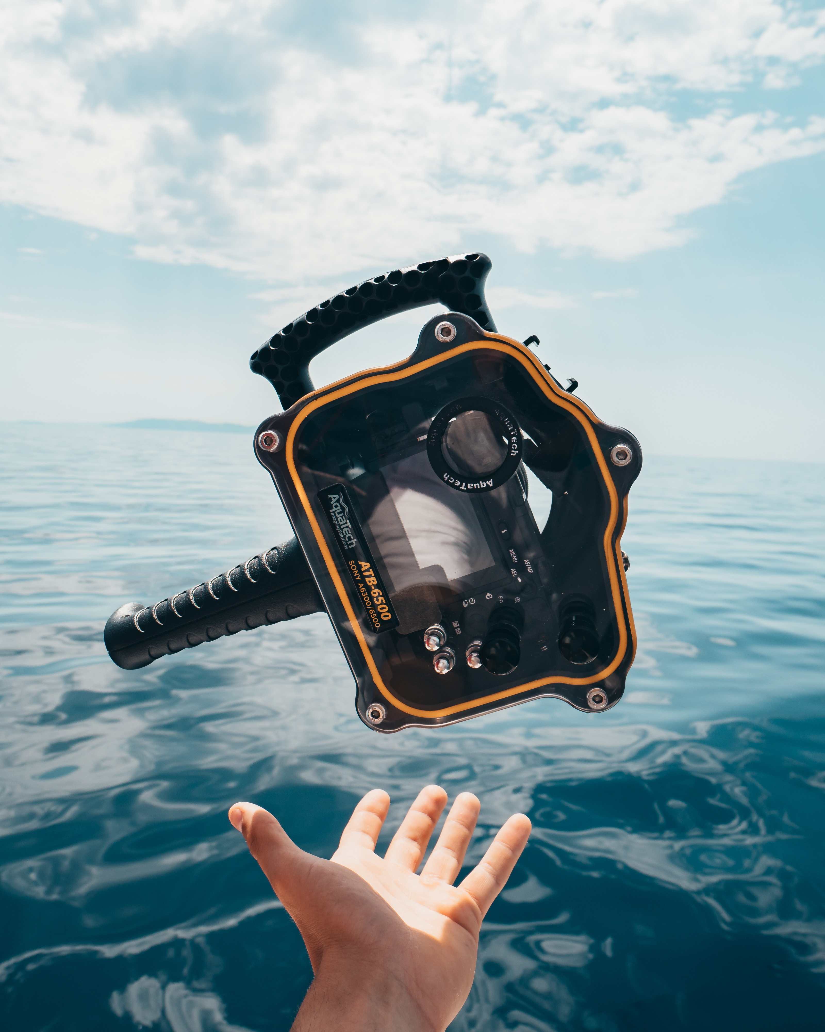 A waterproof underwater camera being thrown into the air above the ocean waters.