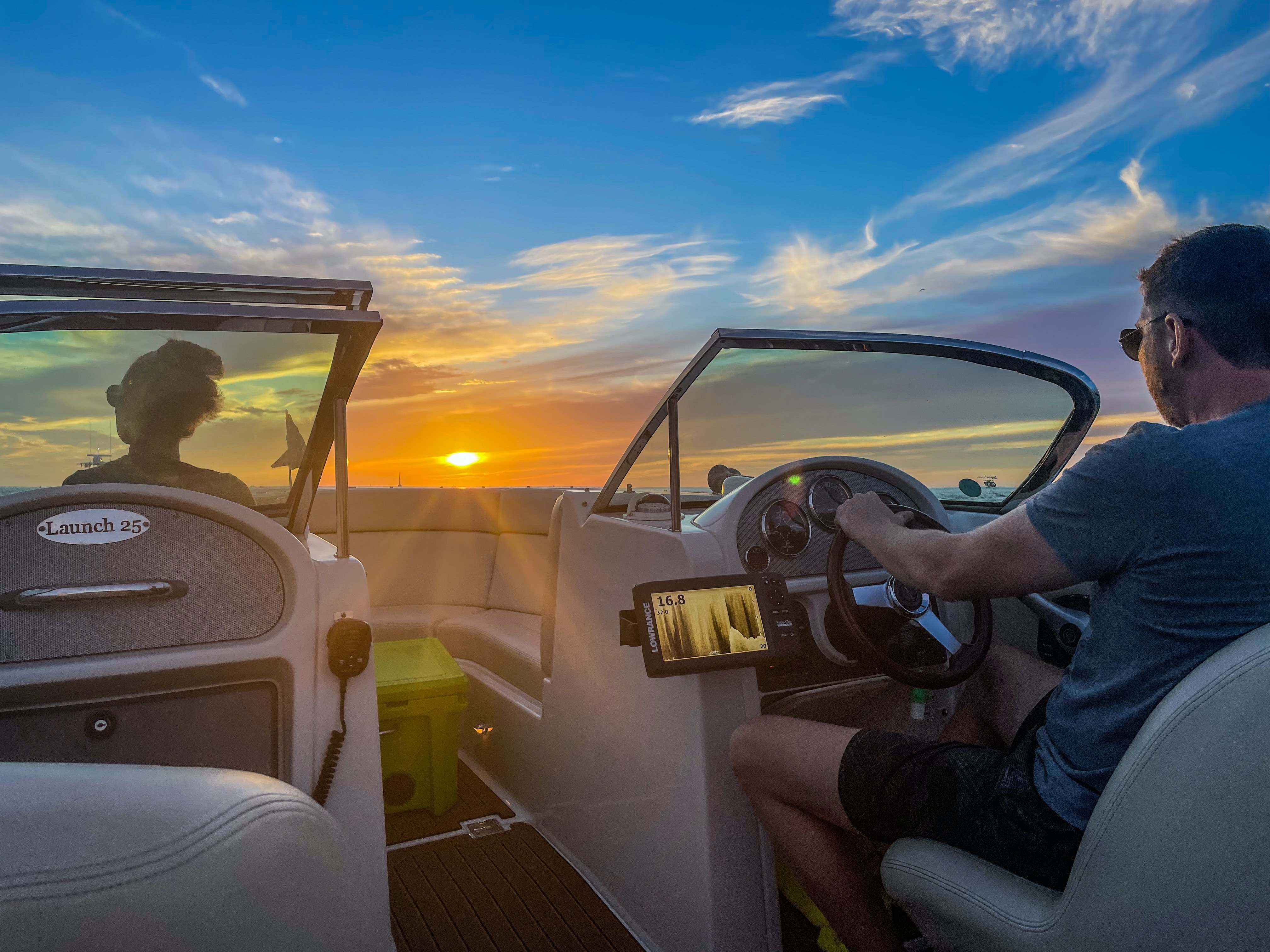 A man steering a boat with an electronic device beside him.