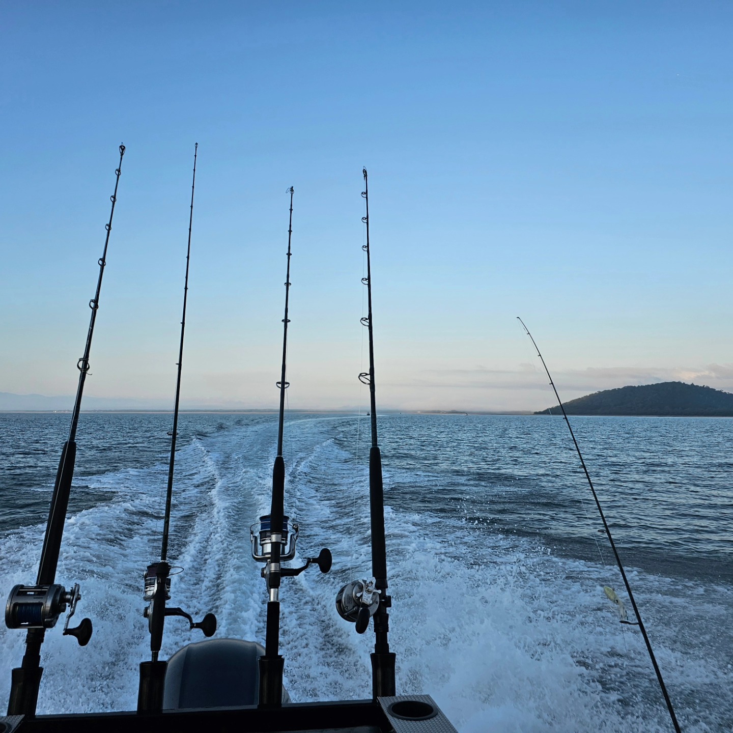 A medium shot of row of trolling fishing rods on a boat at sea.