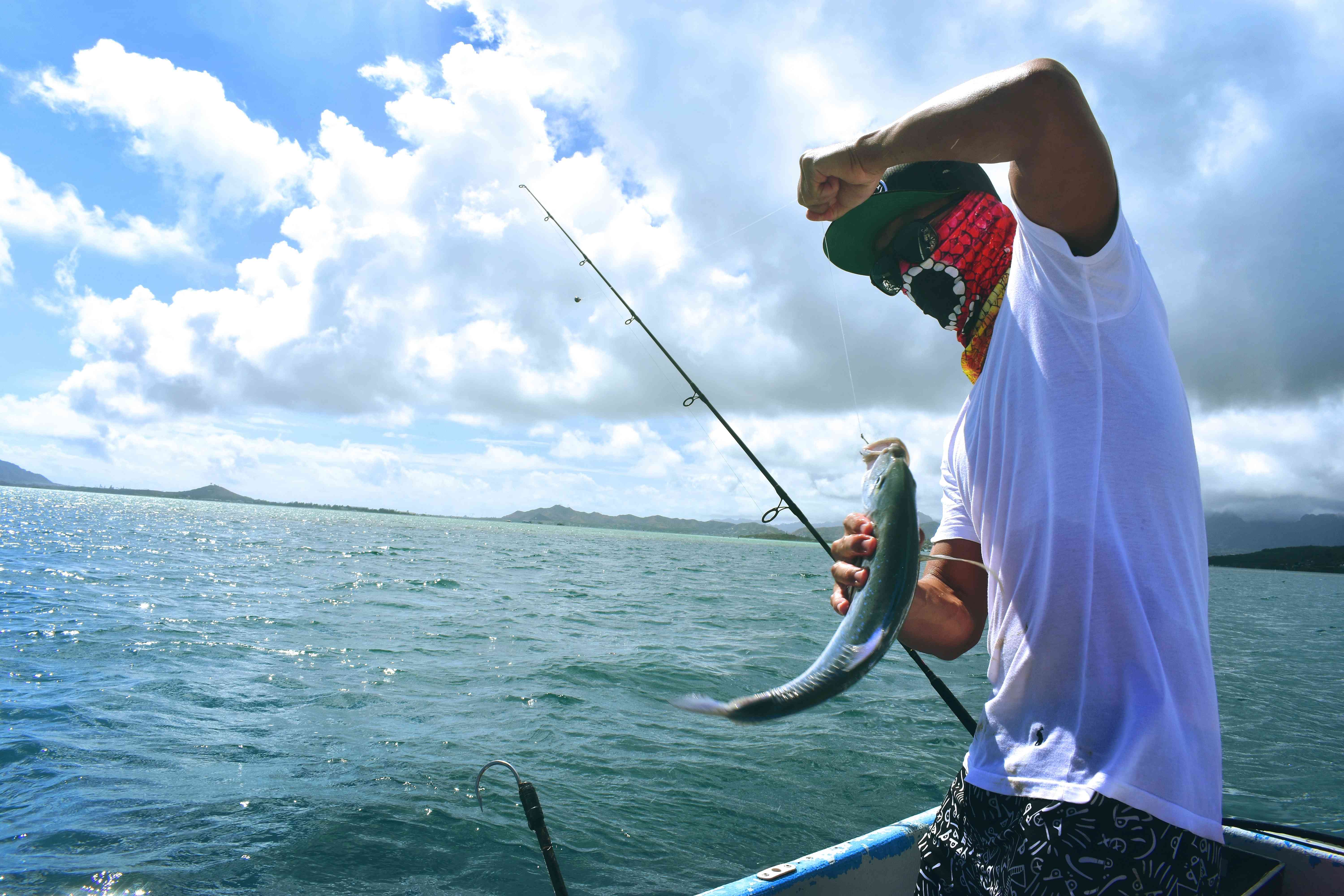 An angler wearing a cap and face mask caught a fish while on a boat.