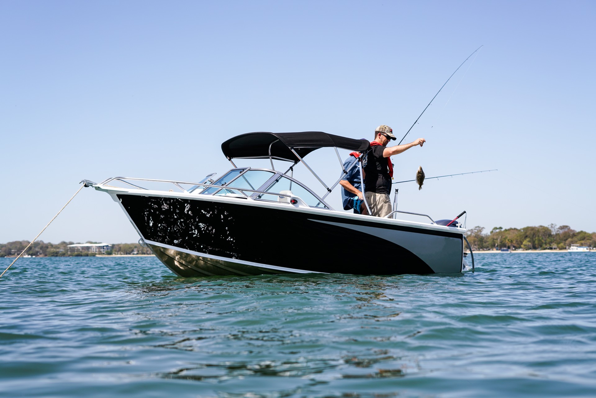 Two men aboard a boat fishing while their boat is anchored on water.