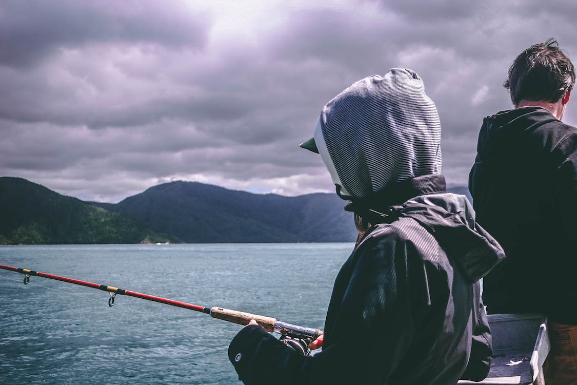 A man in a hood fishing using a rod