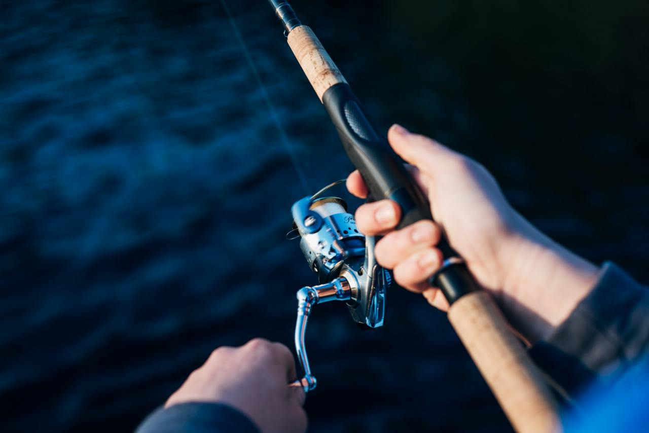 close up picture of someone's hands reeling in a fish using a fishing rod