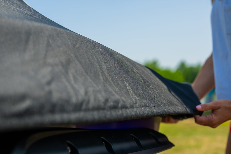 A man covering his boat with a black boat cover.