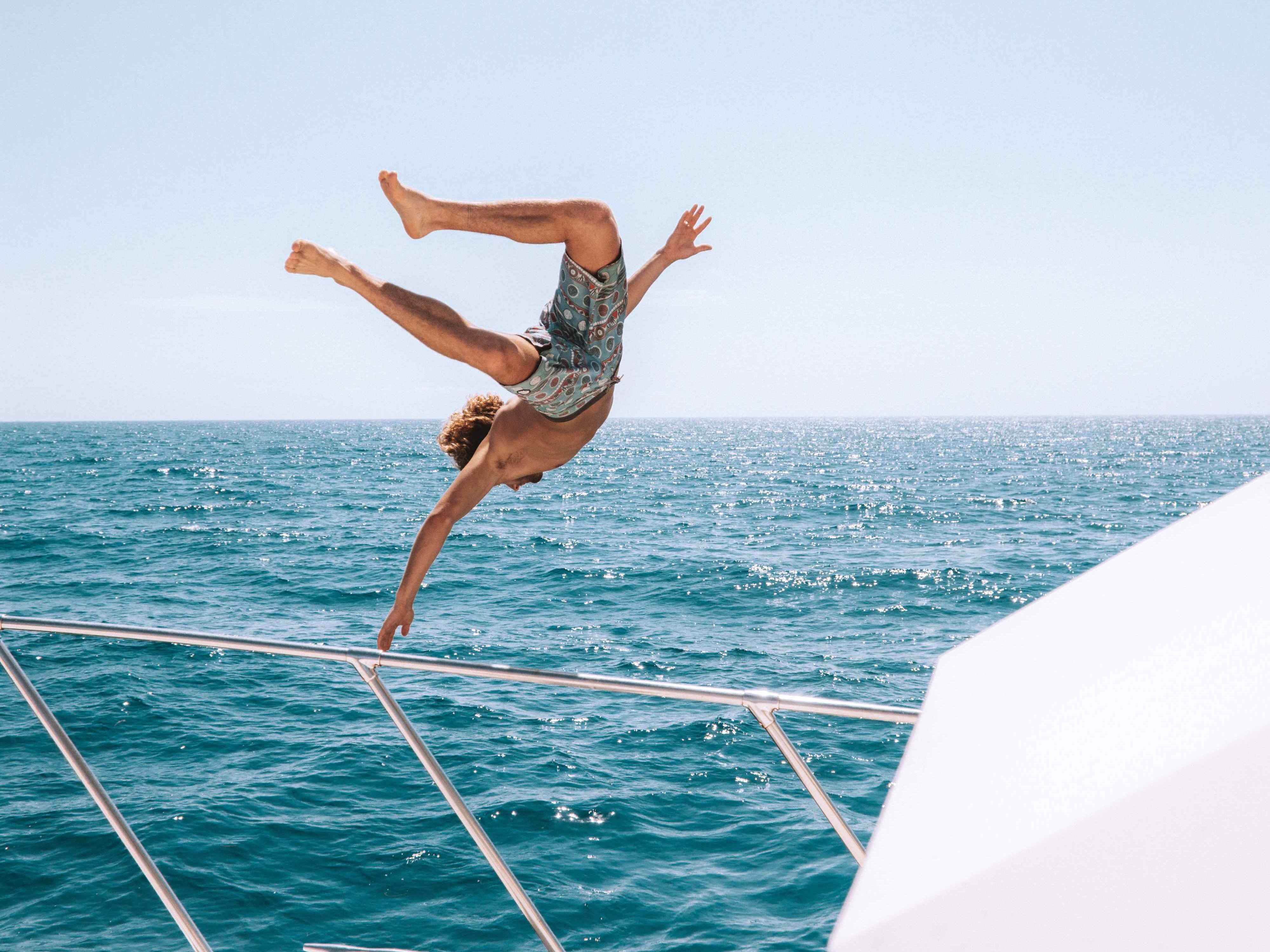 A man jumping off the the railings of a boat into the ocean.