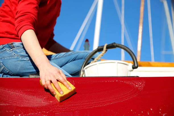 Woman cleaning a boat's hull with a sponge.