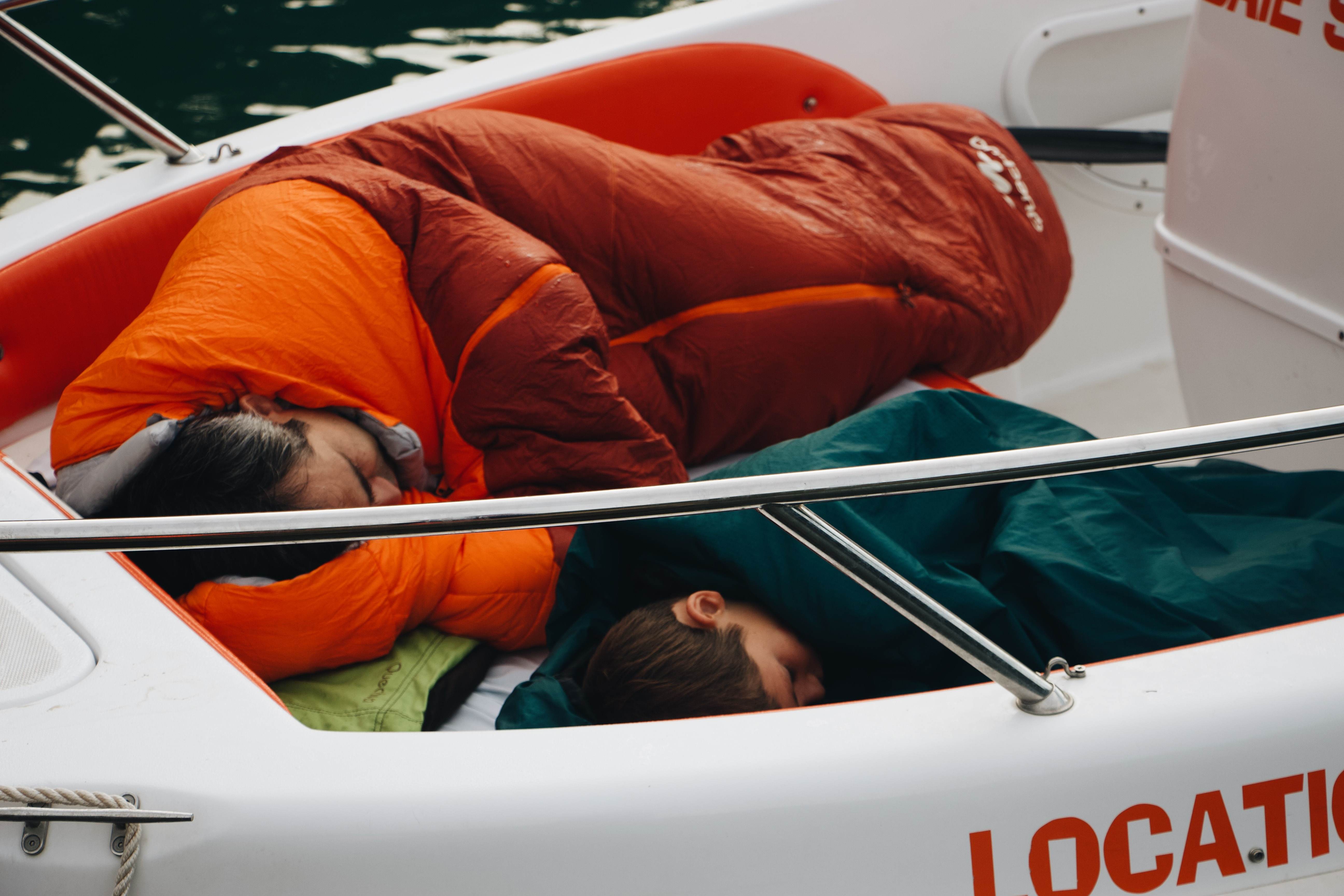 Two people sleeping in sleeping bags on the back area of the boat