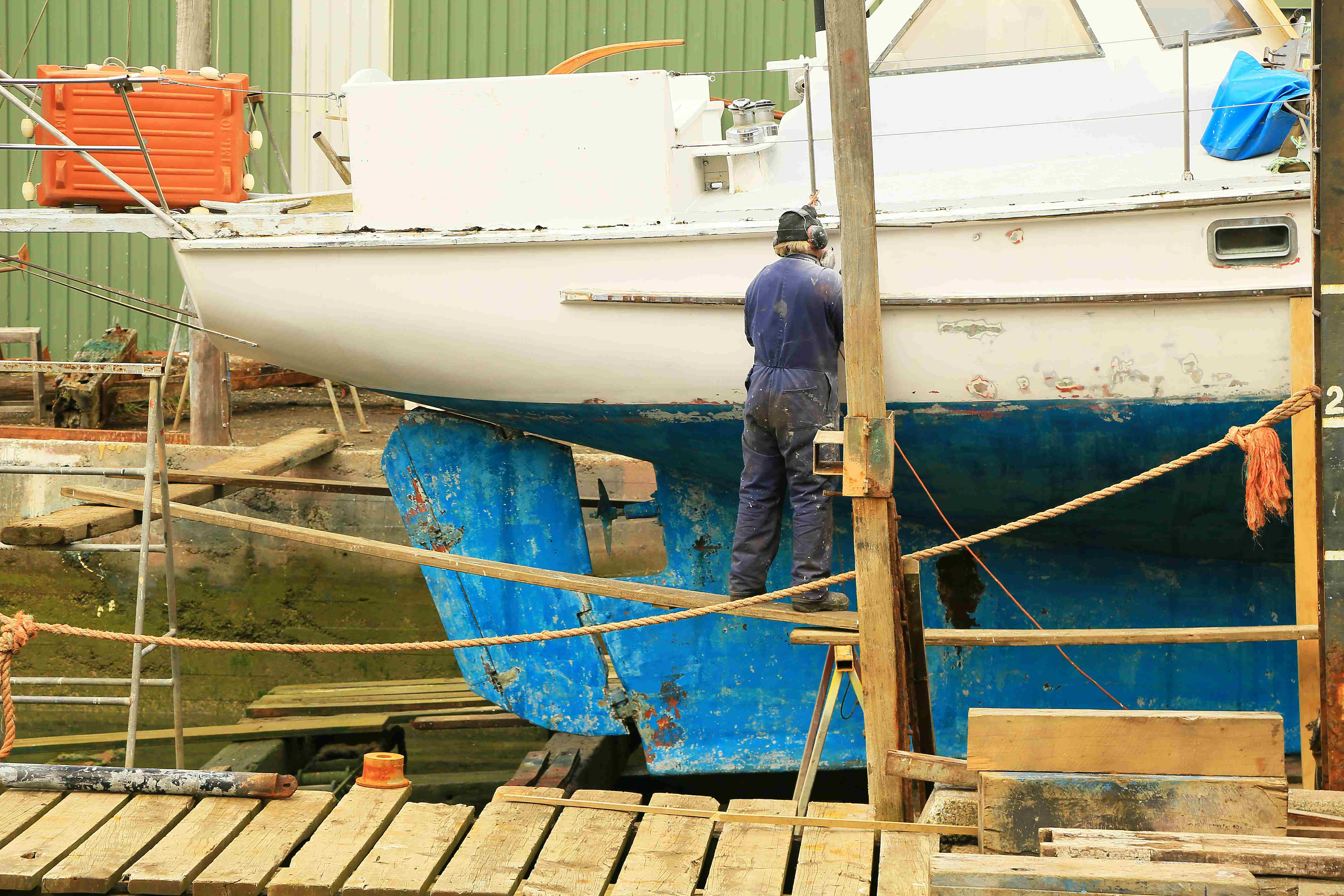 A maintenance man doing maintenance work on a boat's hull.