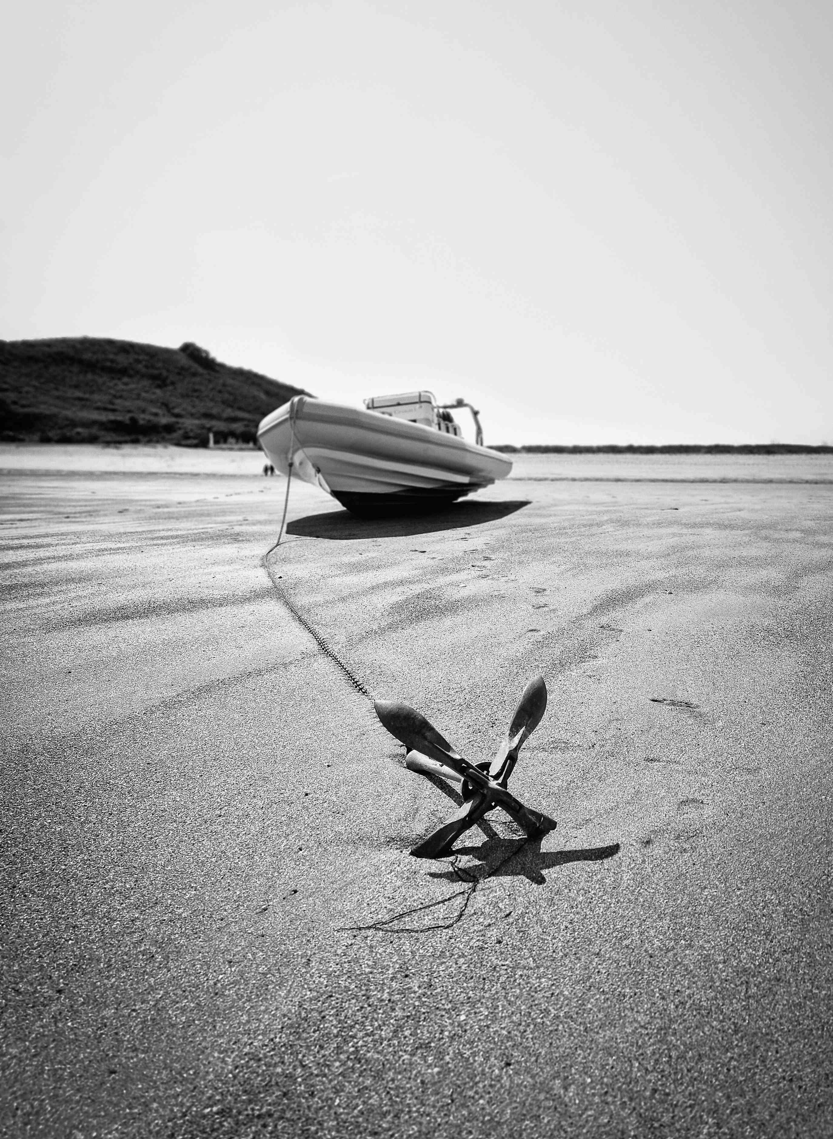 A black and white photo of a small boat anchored on a beach.