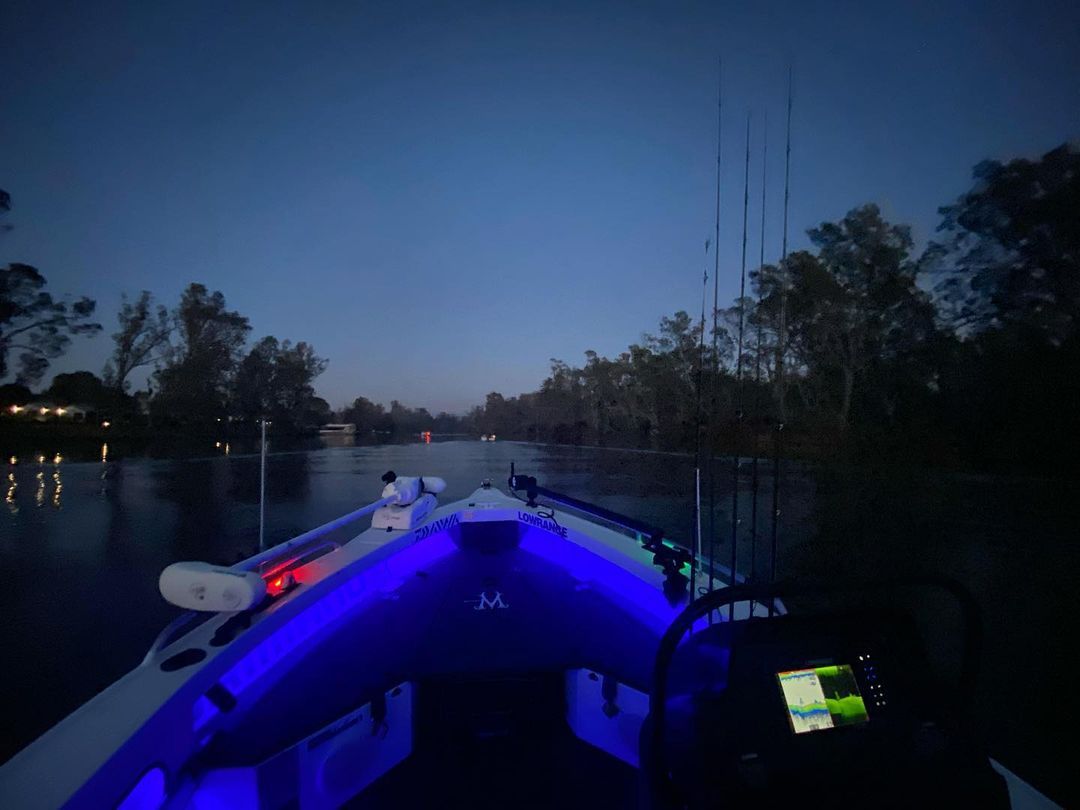 A boat cruising at nighttime while its cabin is illuminated with interior lighting