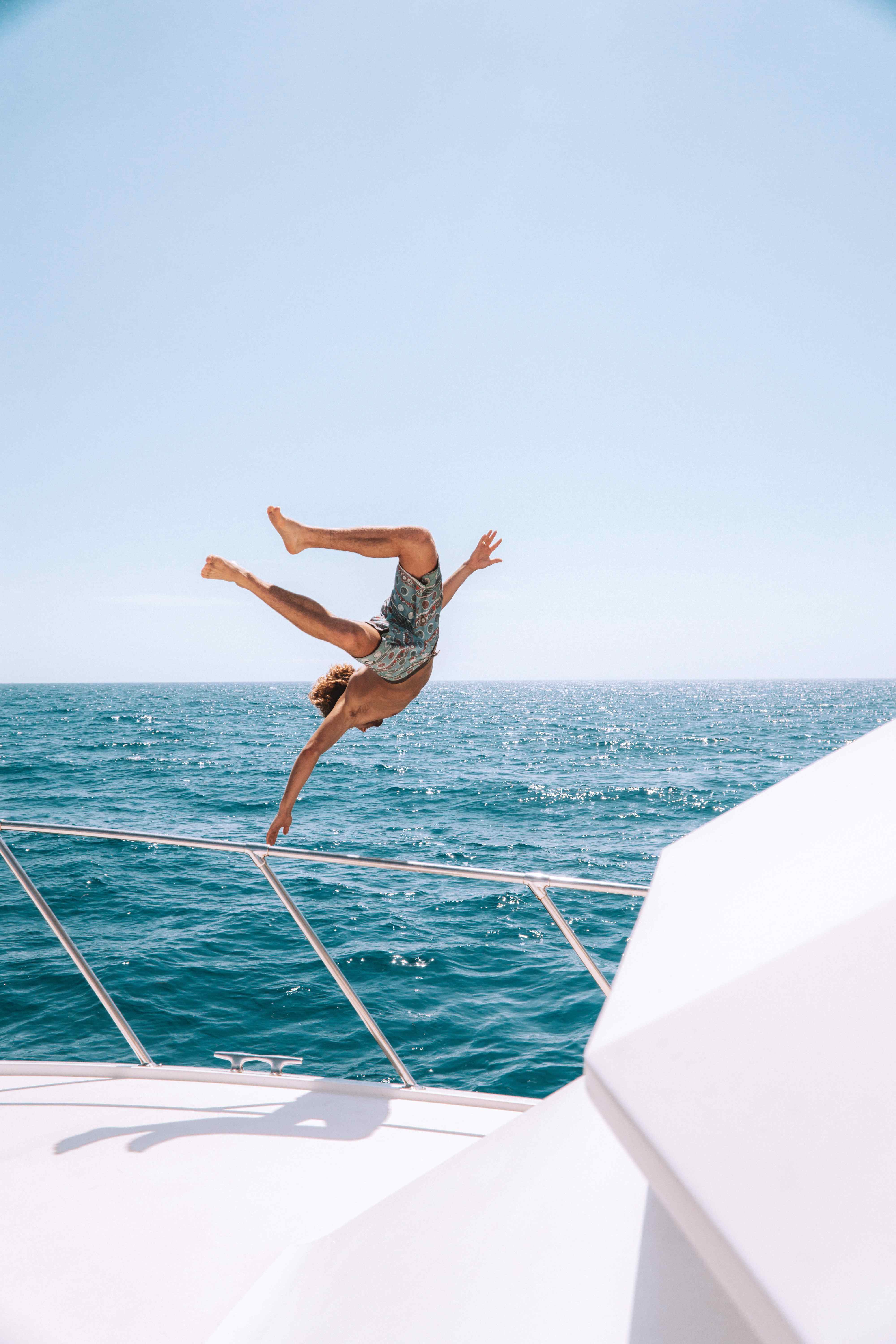 A man jumping off the the railings of a boat into the ocean.