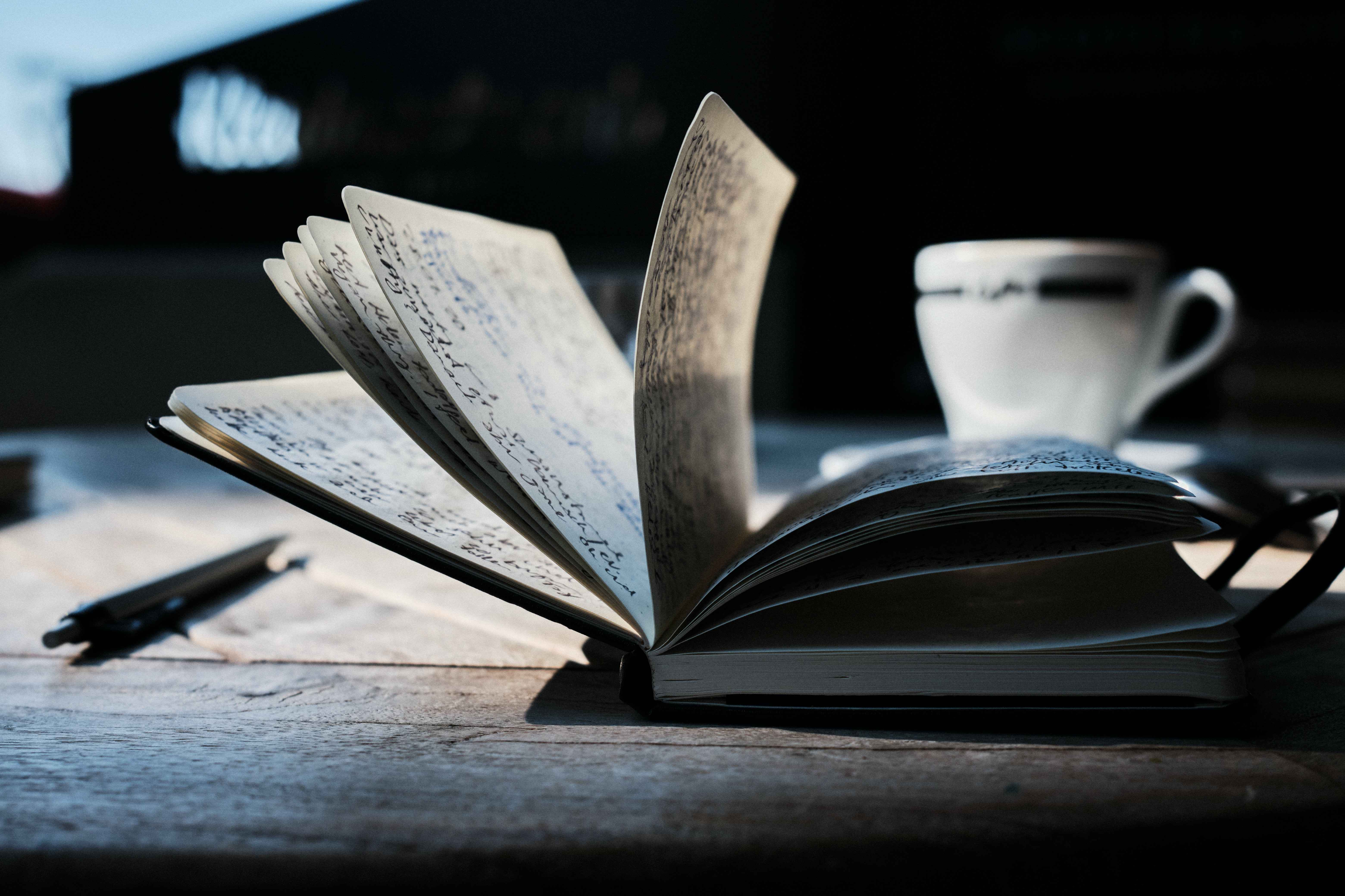 A captain's notebook, pen, and a mug of coffee on top of a wooden table.