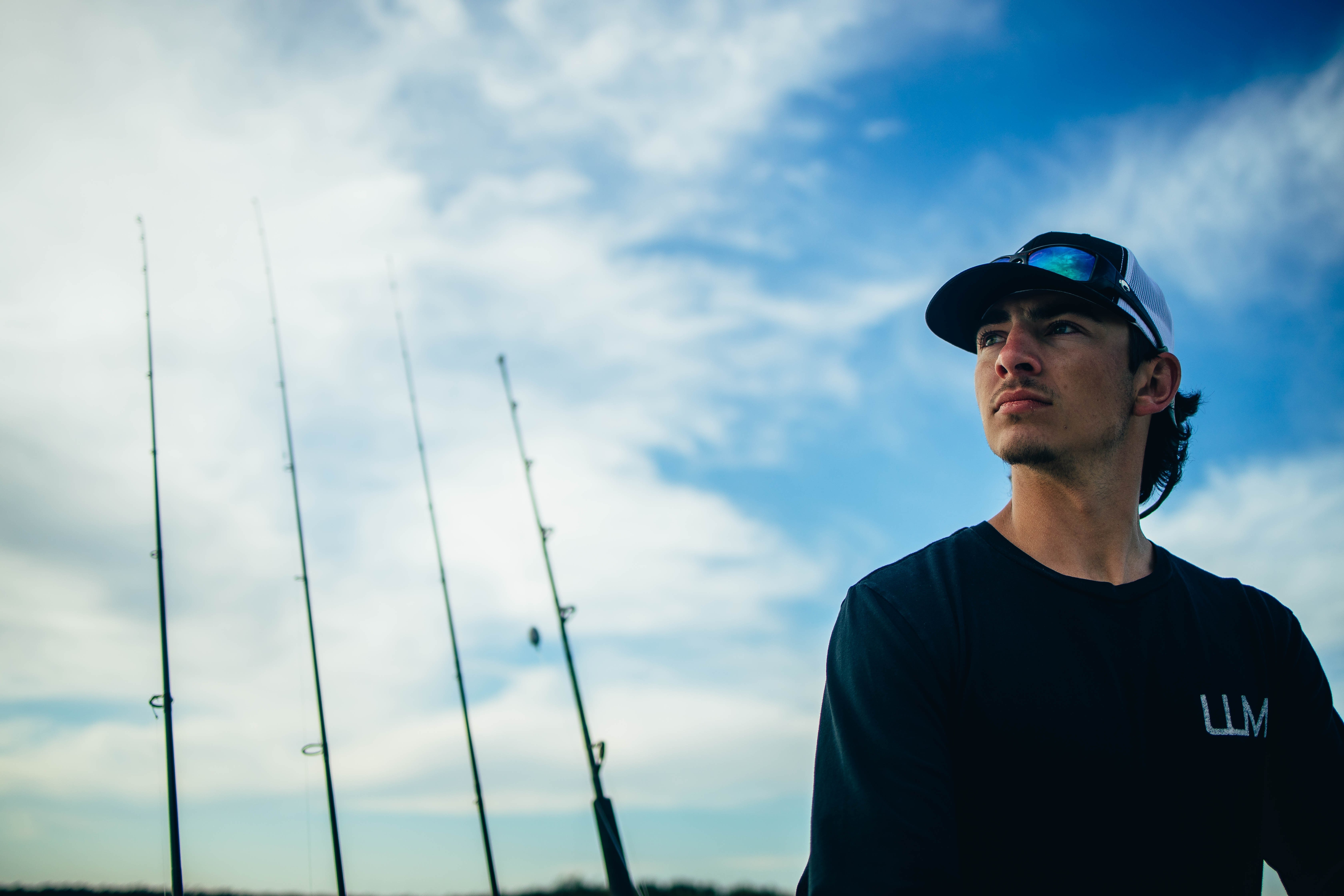 A man wearing a cap is staring off into the distance in deep thought with fishing rods behind him.