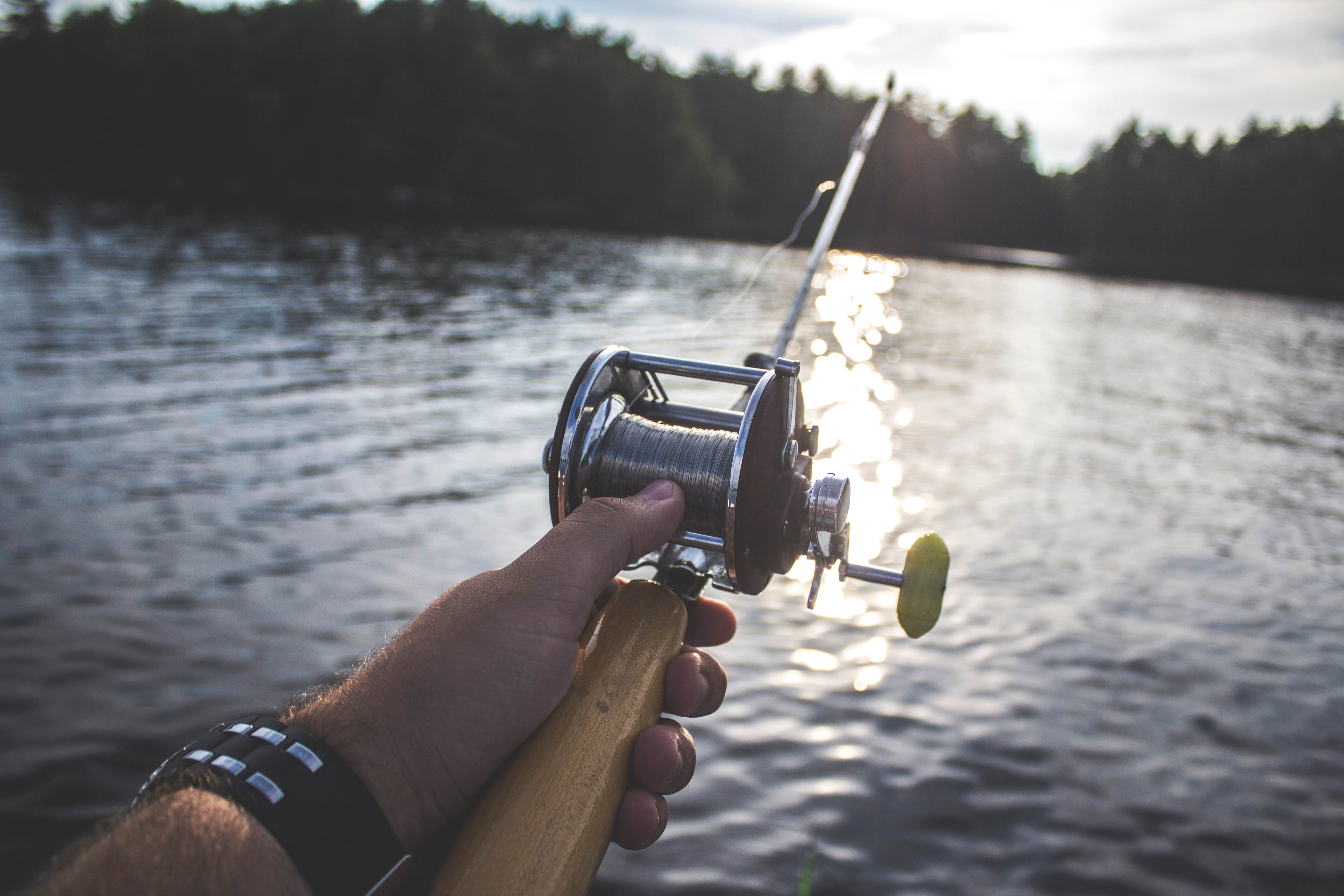 A close up of a hand holding a fishing rod on a body of water.