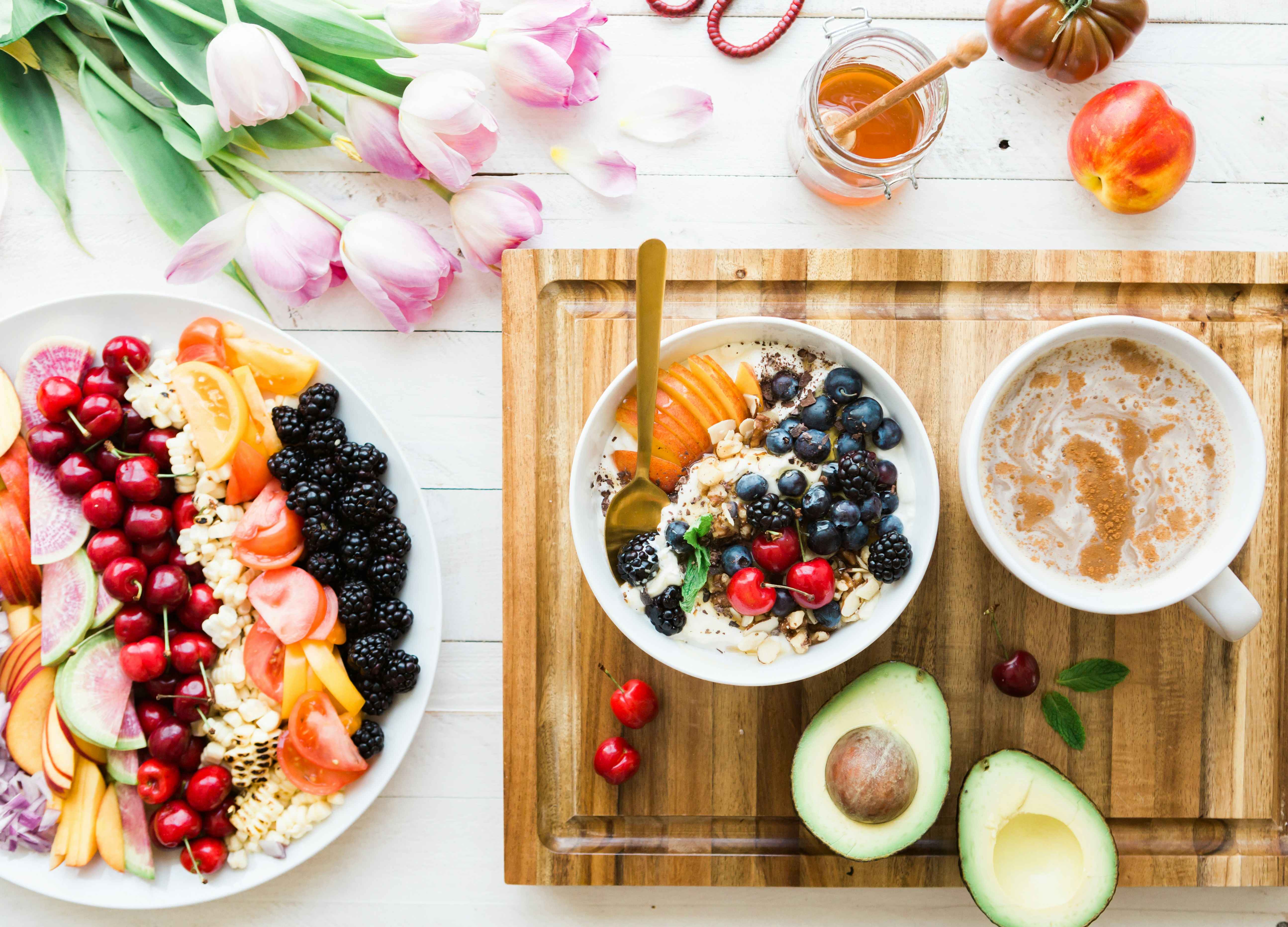 Healthy food consisting of fruits, wheat, and honey with pink tulips as decor.