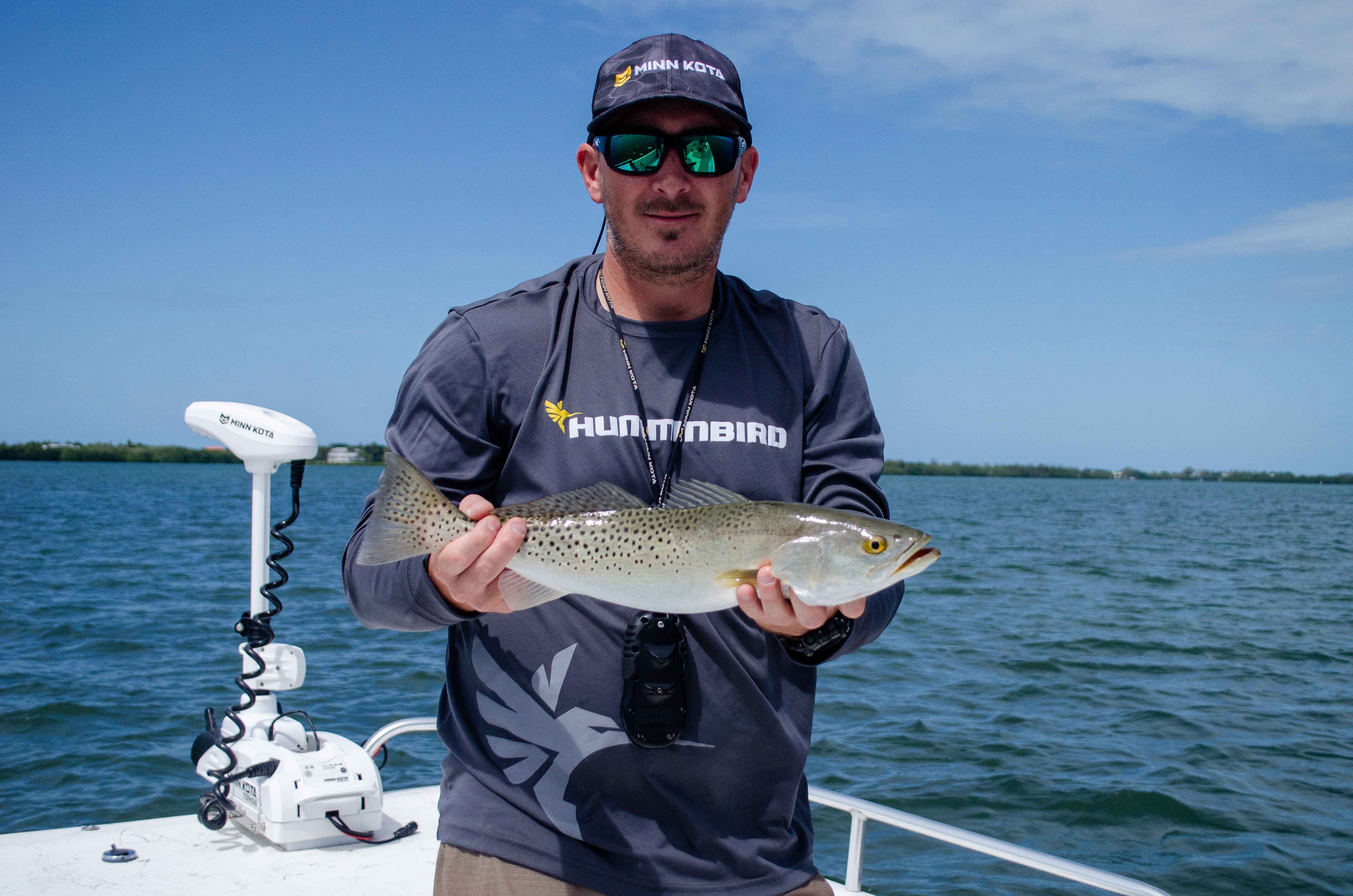 A Minn Kota trolling motor behind a man posing for a photo while holding fish.