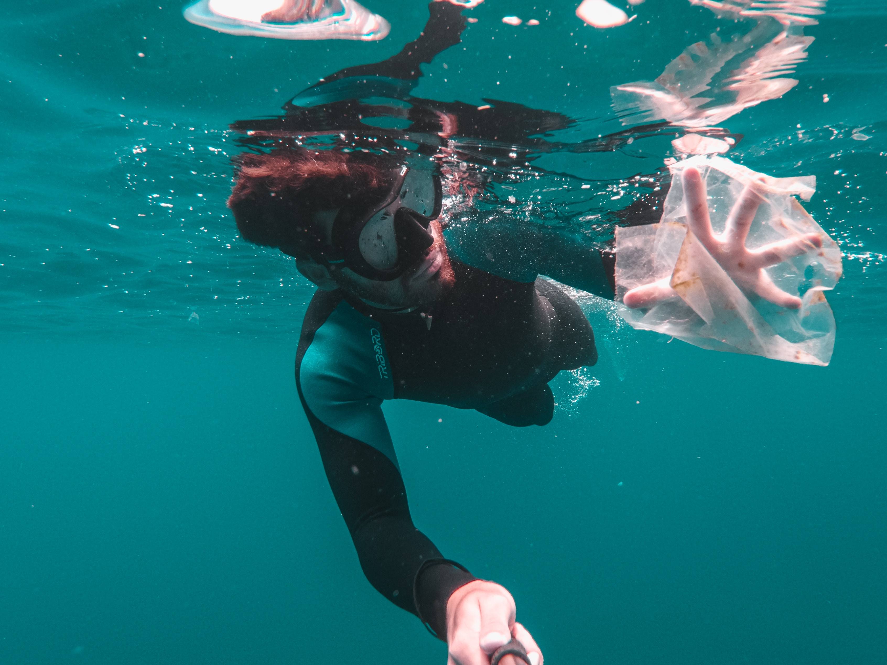 A diver capturing a floating plastic in the ocean.