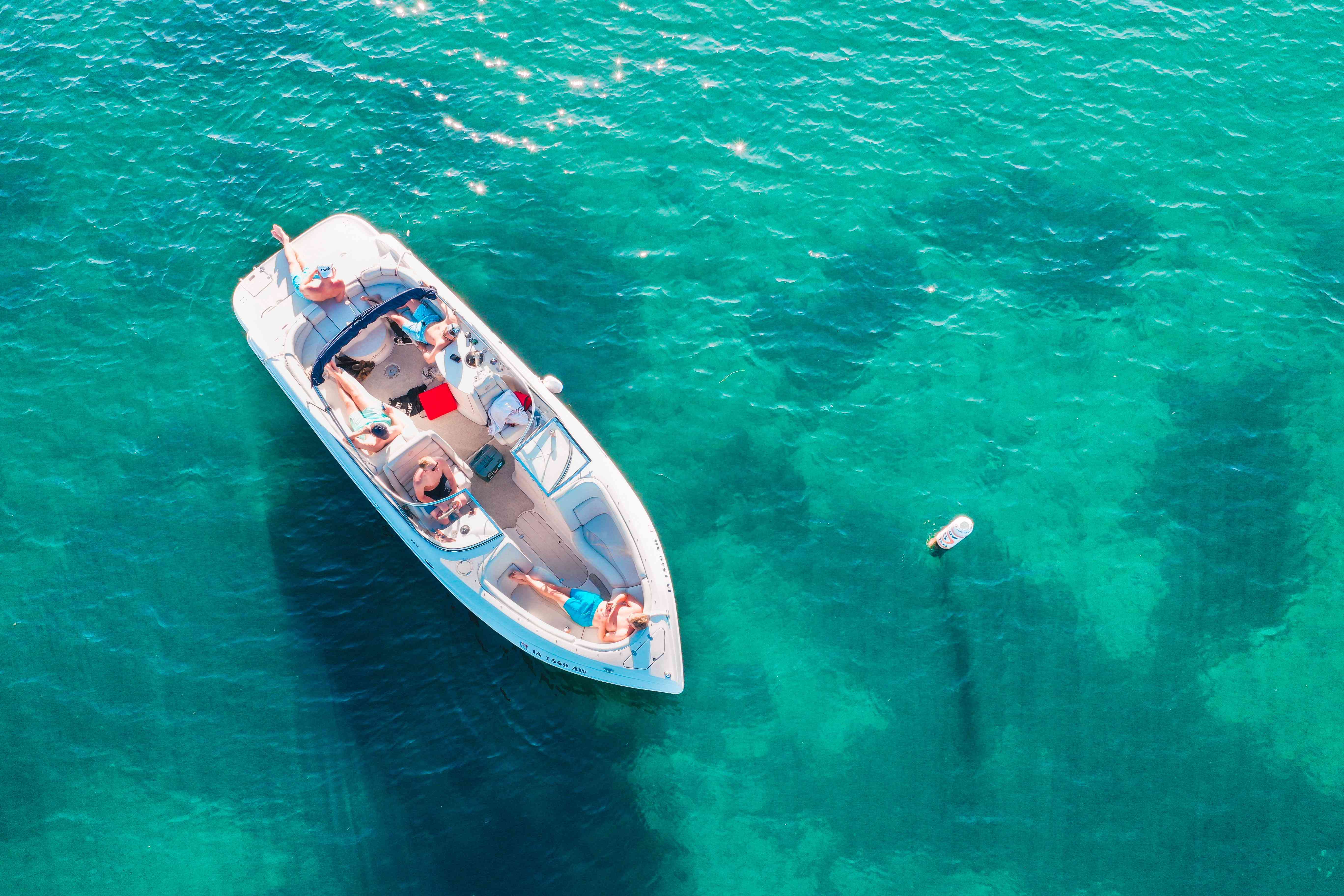 A group of young people sprawled out on an open boat that is anchored on a body of water.