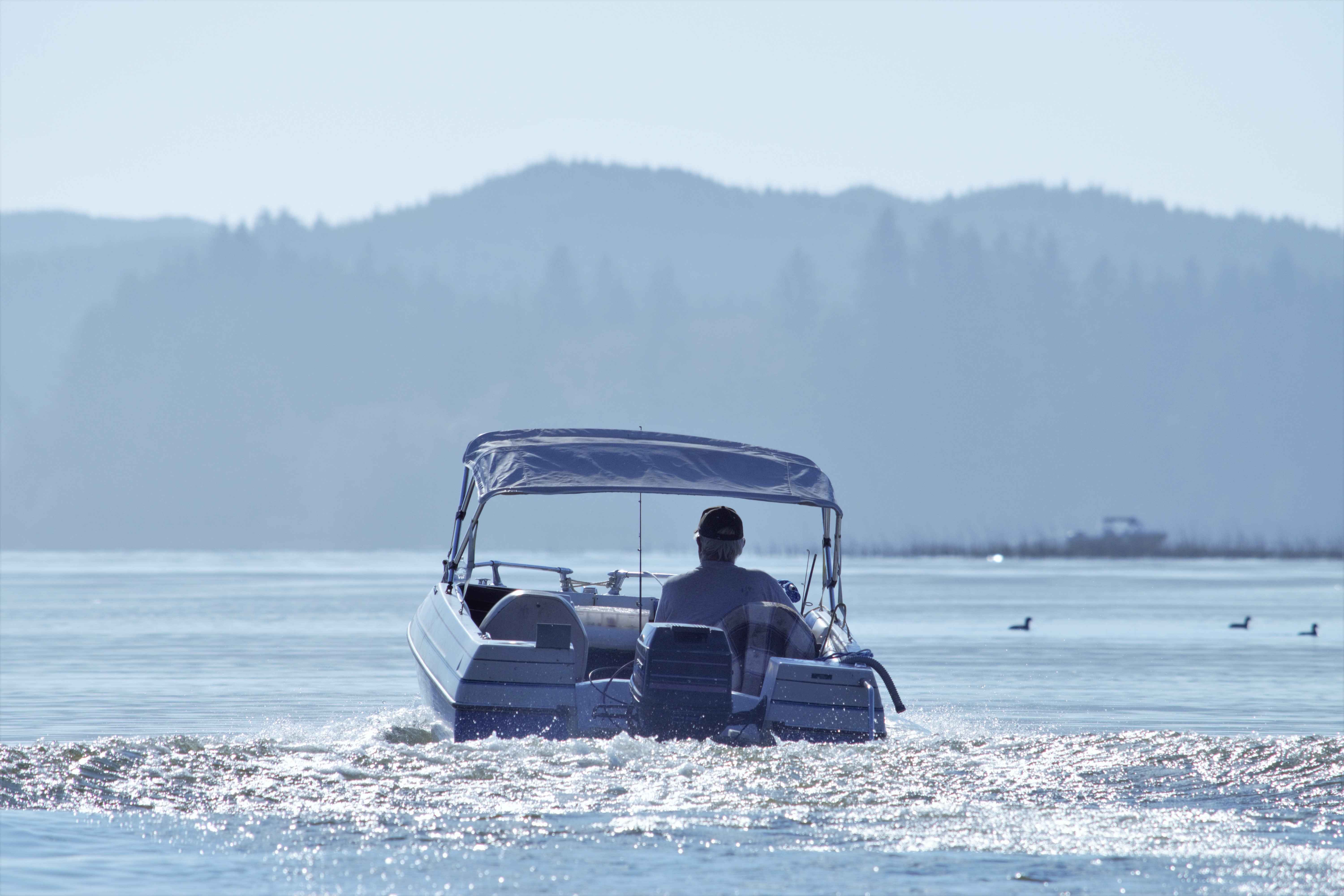 A man operating a boat with a Bimini top alone.