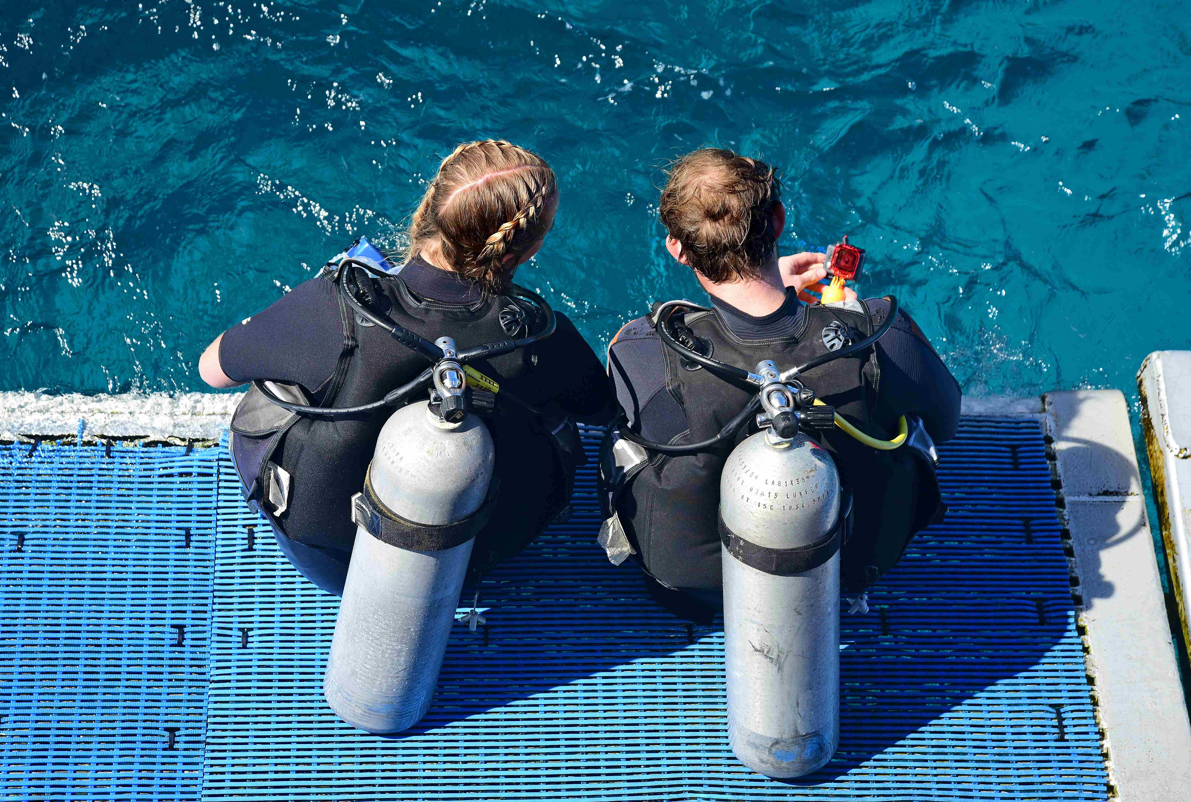 Two young people wearing scuba suits sitting on a diving ramp.