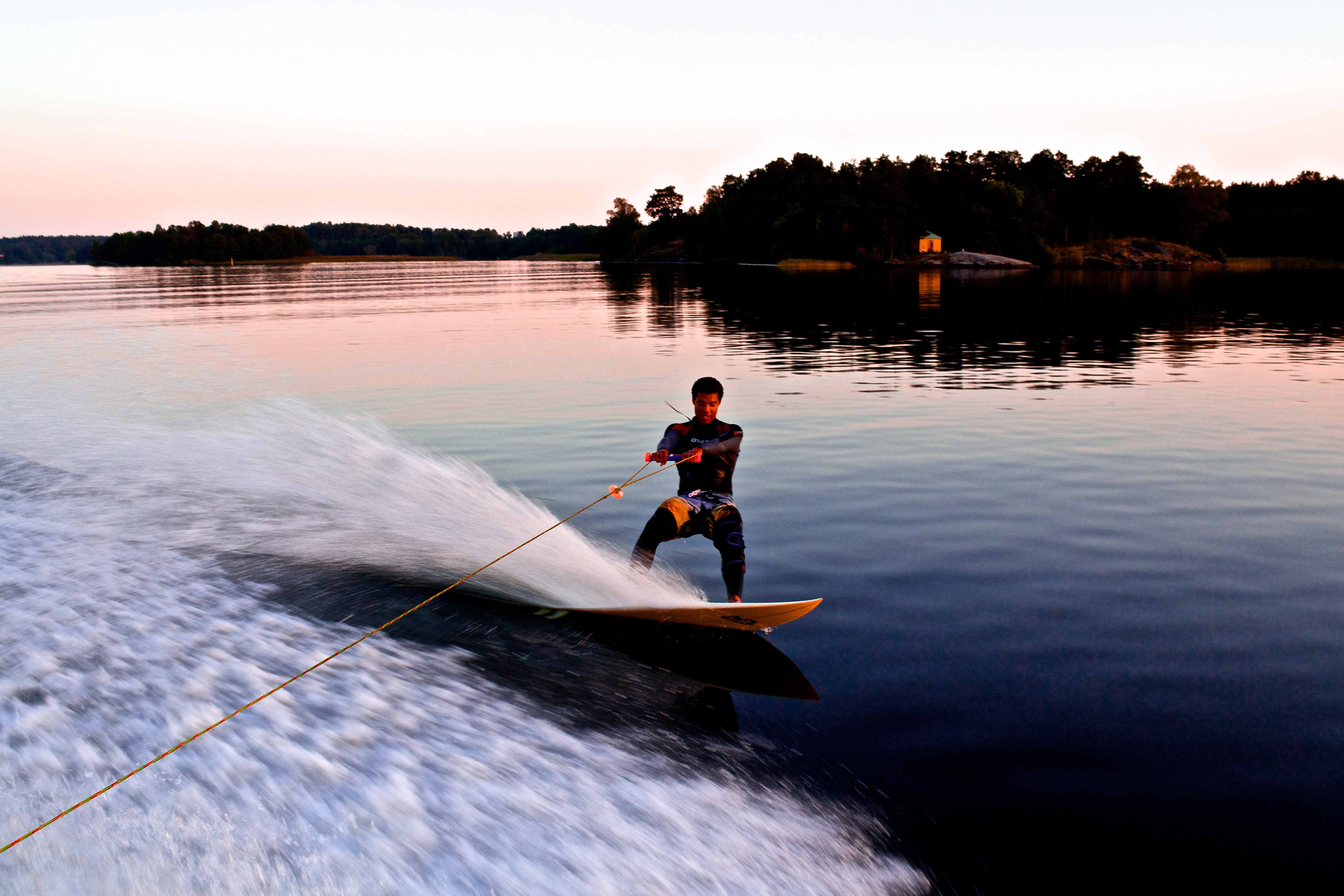 A rider on a wakeboard holding to a rope is towed on a lake.