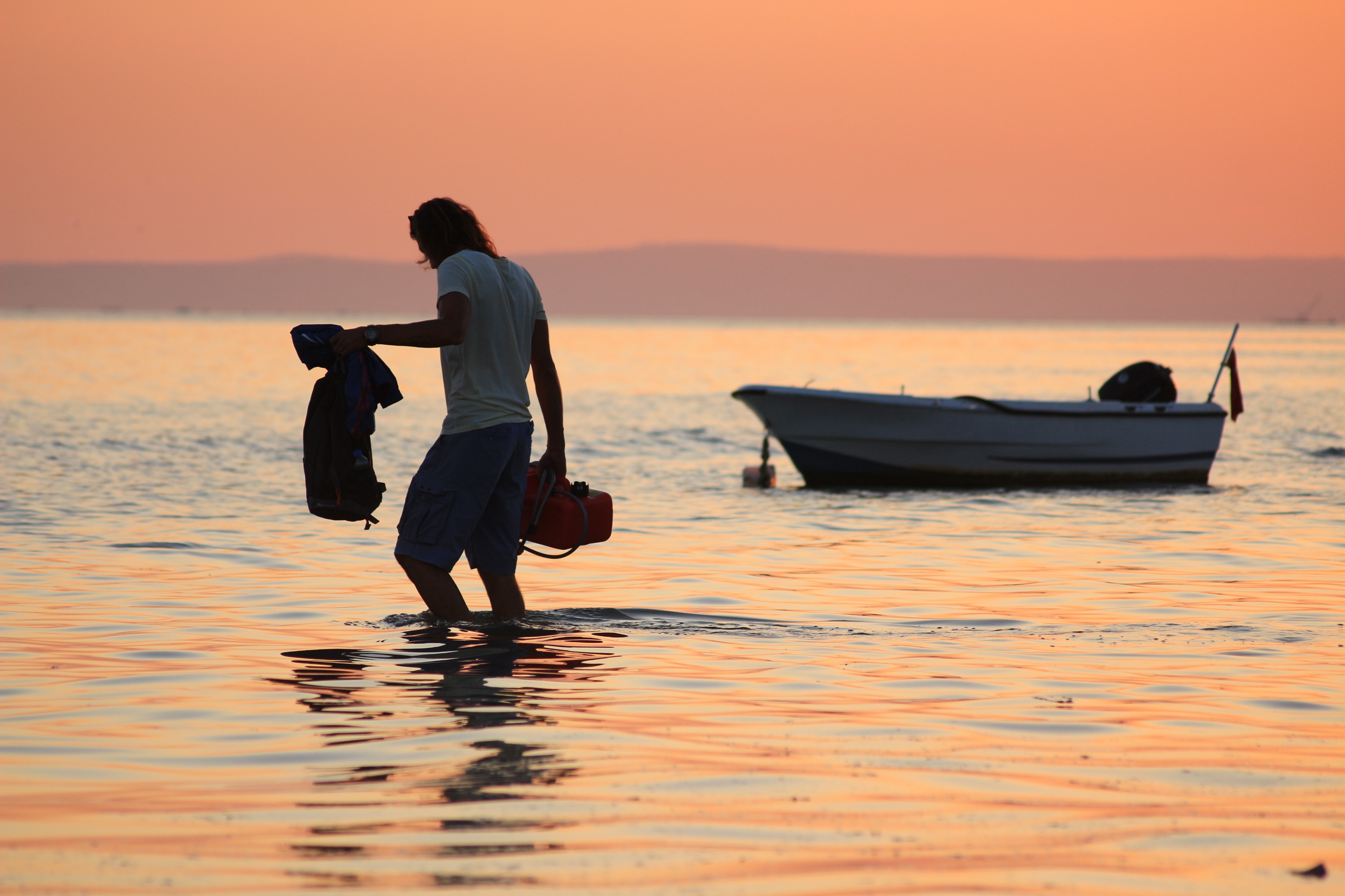 A man on the shore making his way to a tinnie boat anchored up ahead of him.