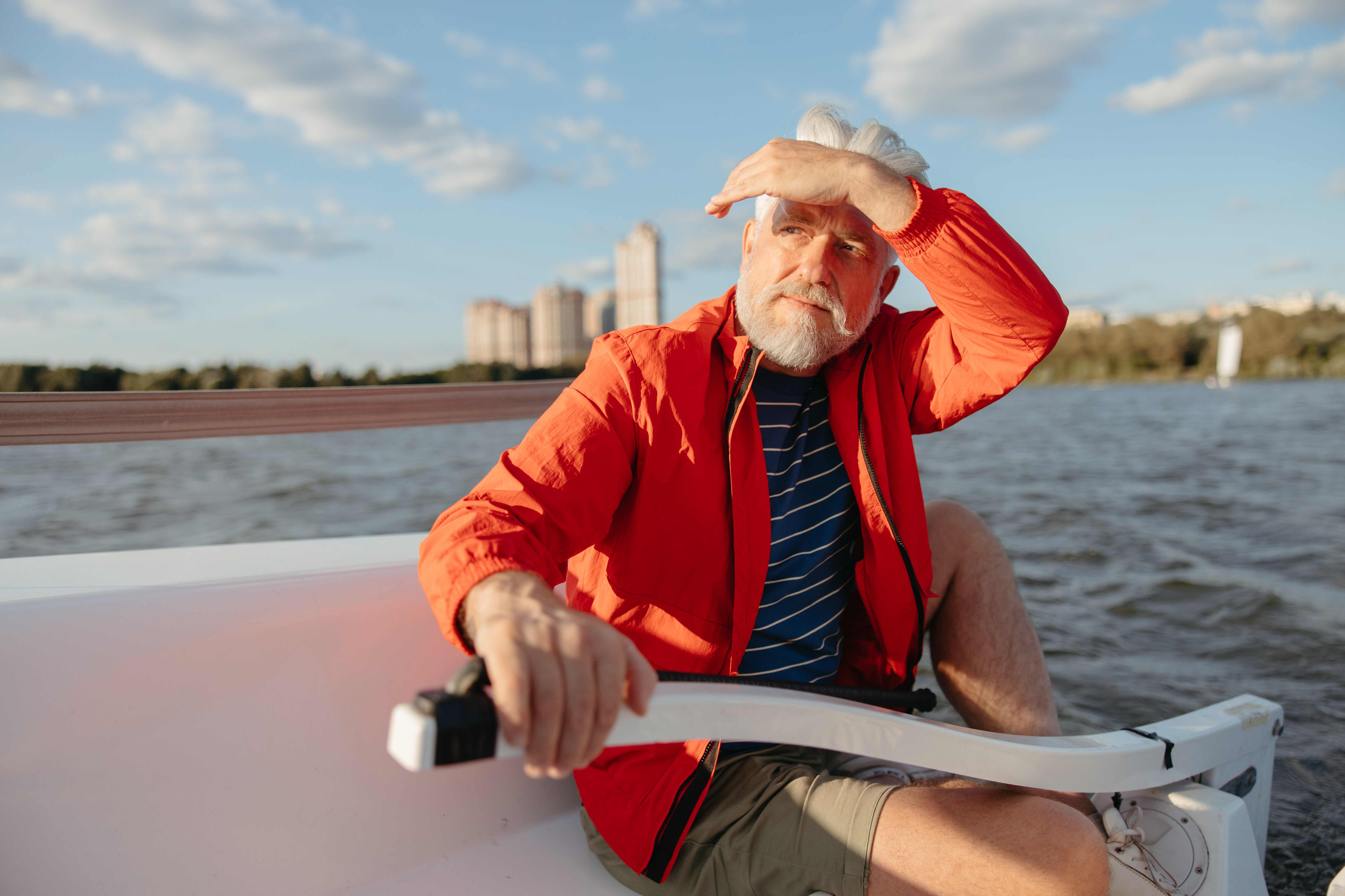 An elderly man wearing a bright orange jacket is steering the boat.