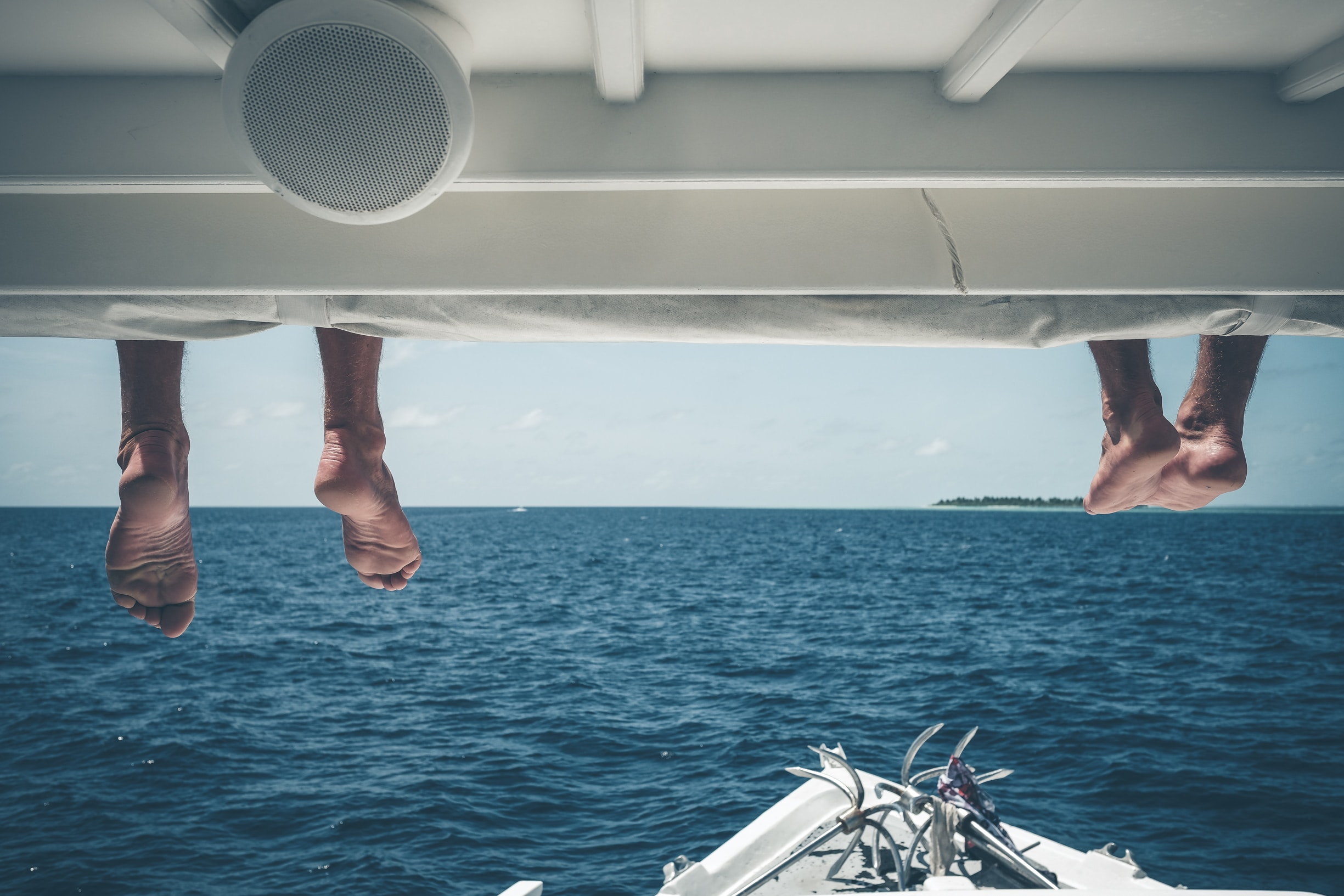 Two pair of legs hanging on a boat's roof while being on a water excursion.