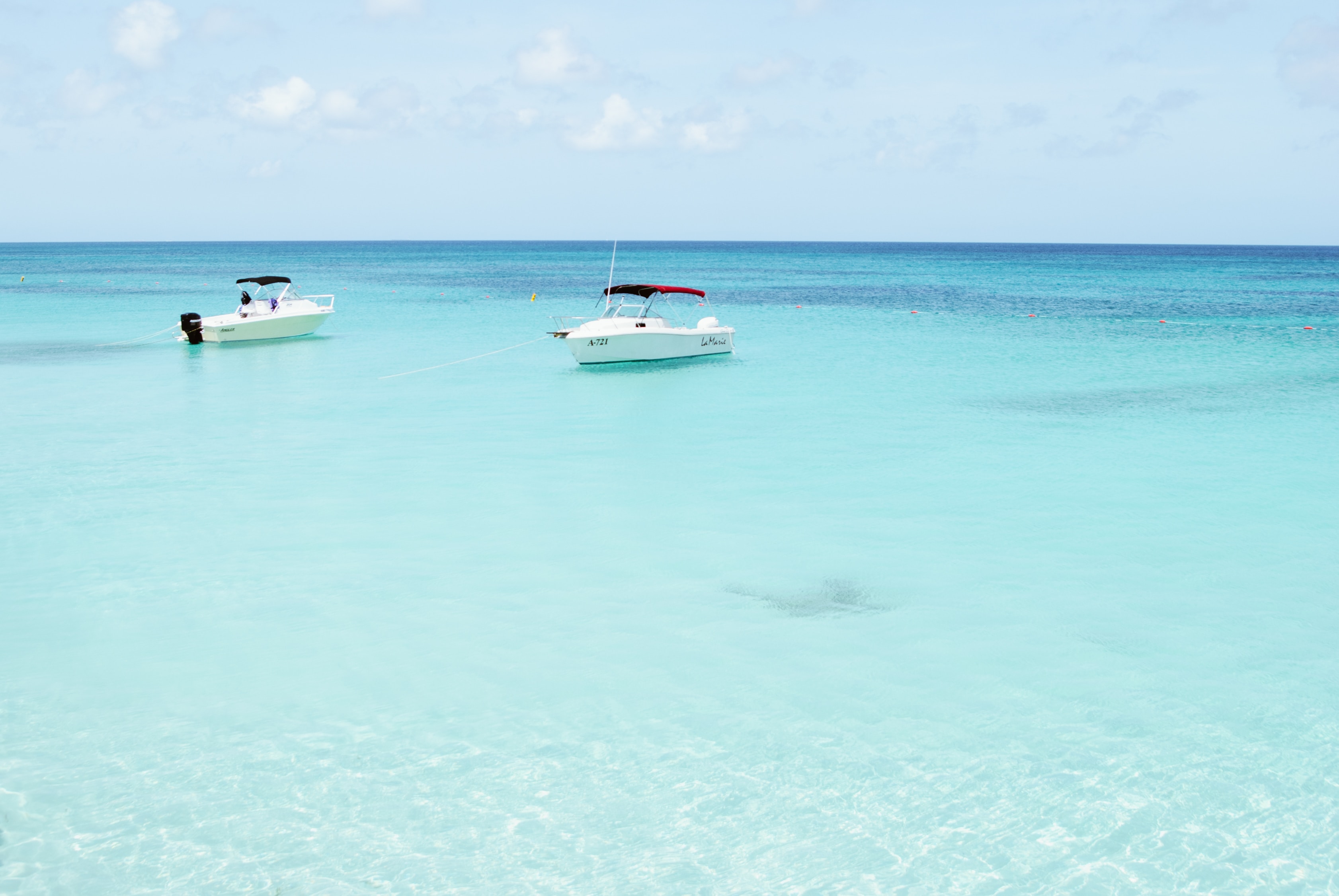 2 boats anchored in a shallow area at sea.