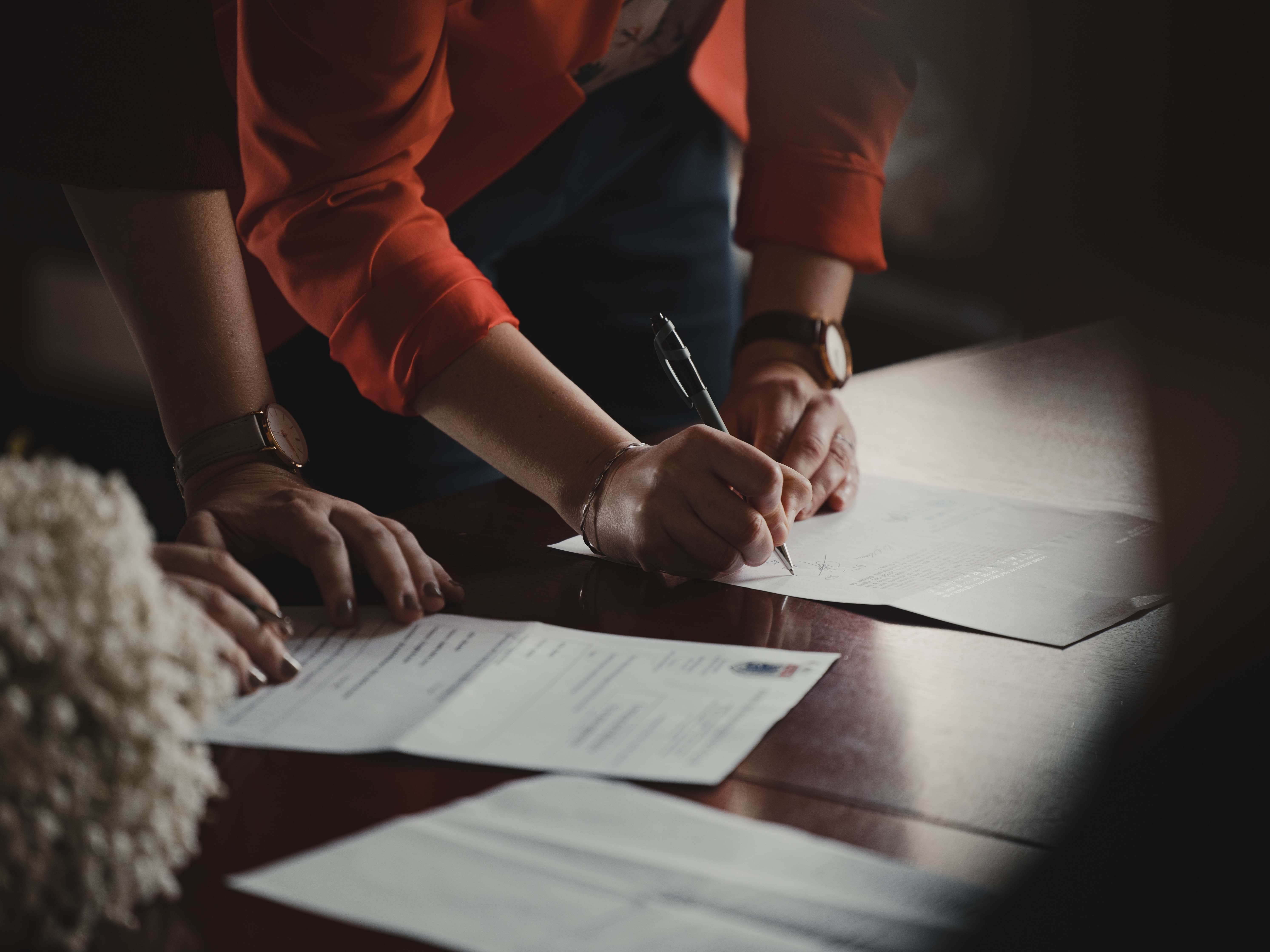 A oerson wearing an orange shirt signing a form.