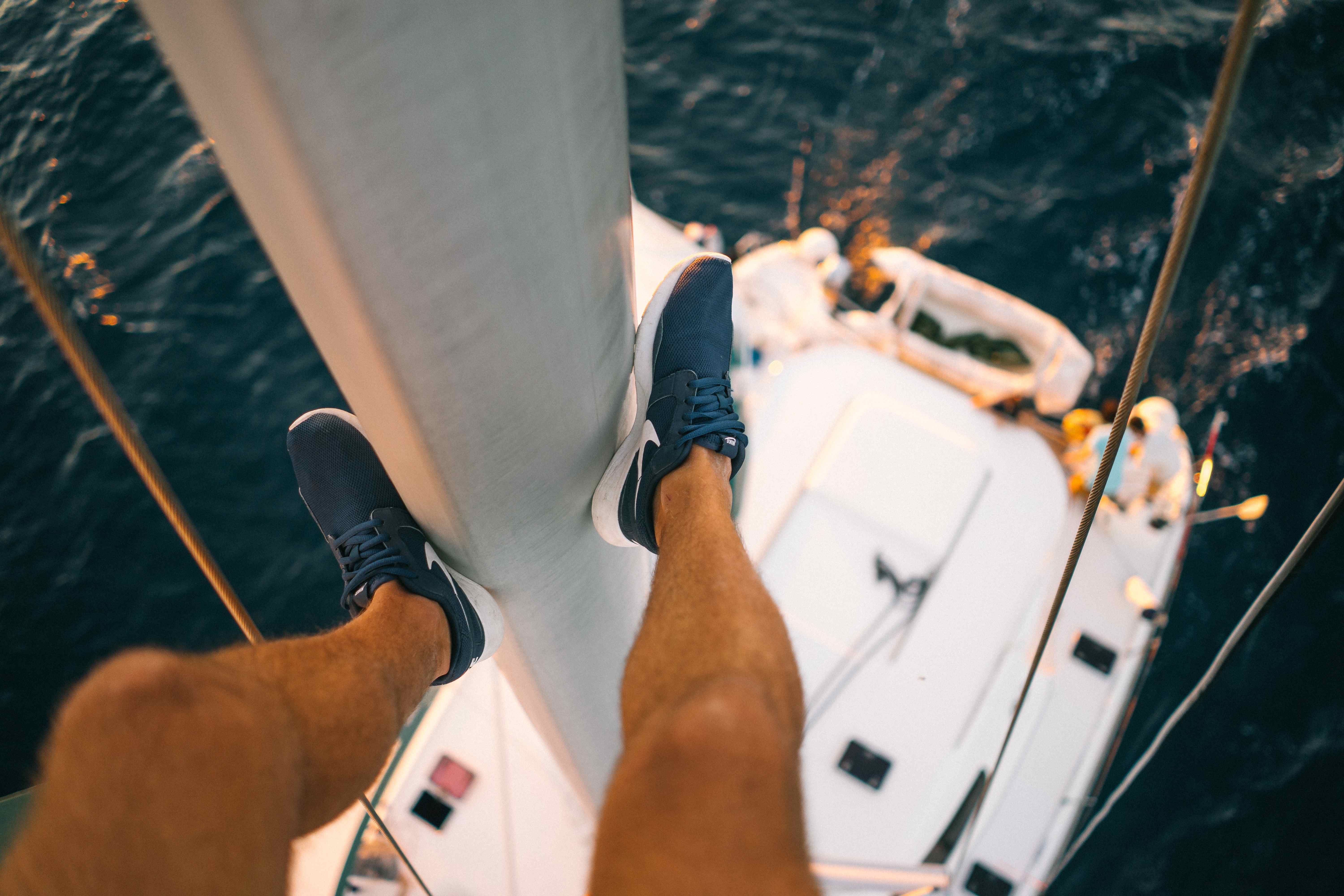 A bird's eye view of a boat's mast pole and a pair of legs wearing blue sneakers.