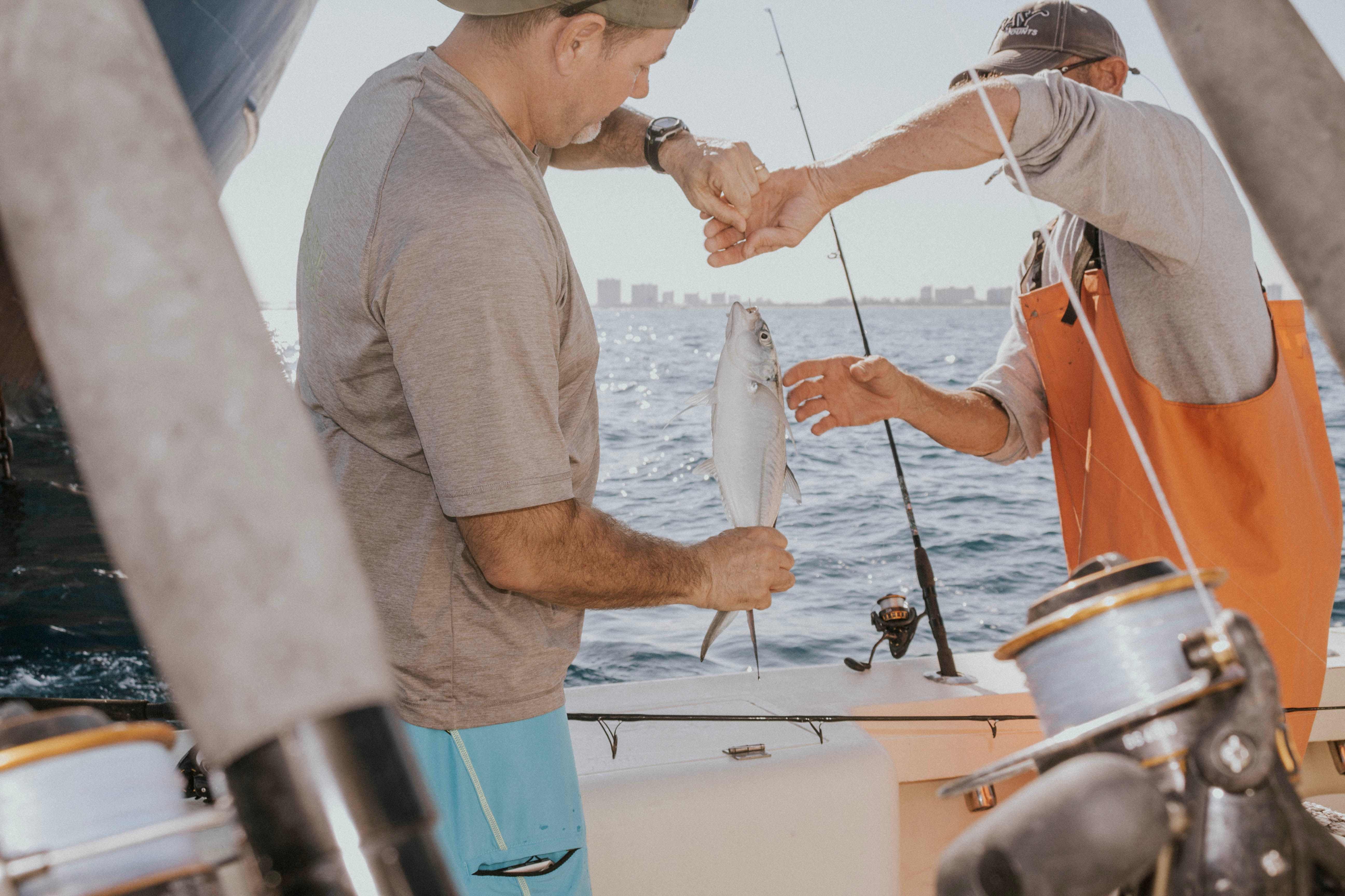 Two anglers on a boat help each other handle a fish they caught.