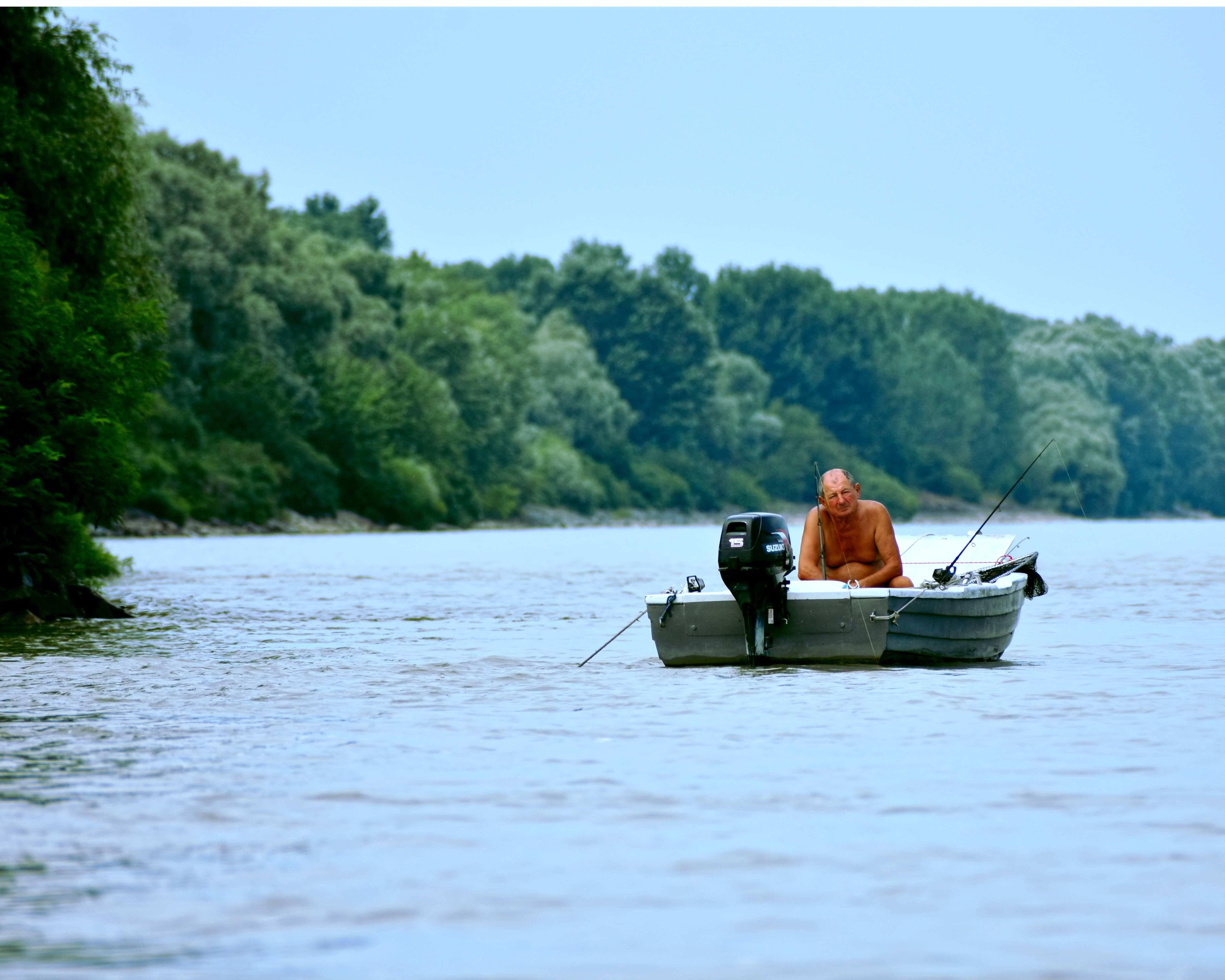 A fisherman sitting on an small open boat with an outboard motor attached on a lake.